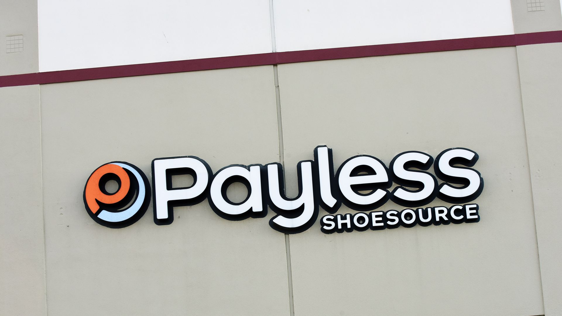 In this image, the orange and white storefront sign for Payless ShoeSource is visible against a beige concrete wall. 