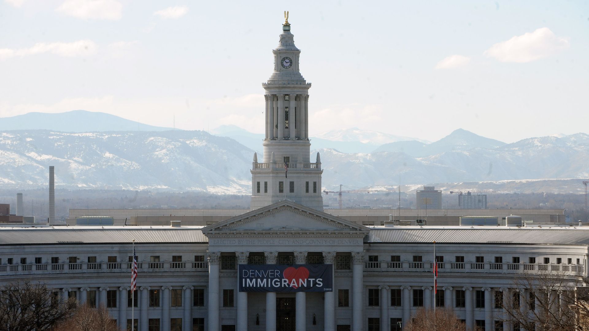 A classical building with a high tower and a sign on its lower column with the word DENVER HEARTS IMMIGRANTS