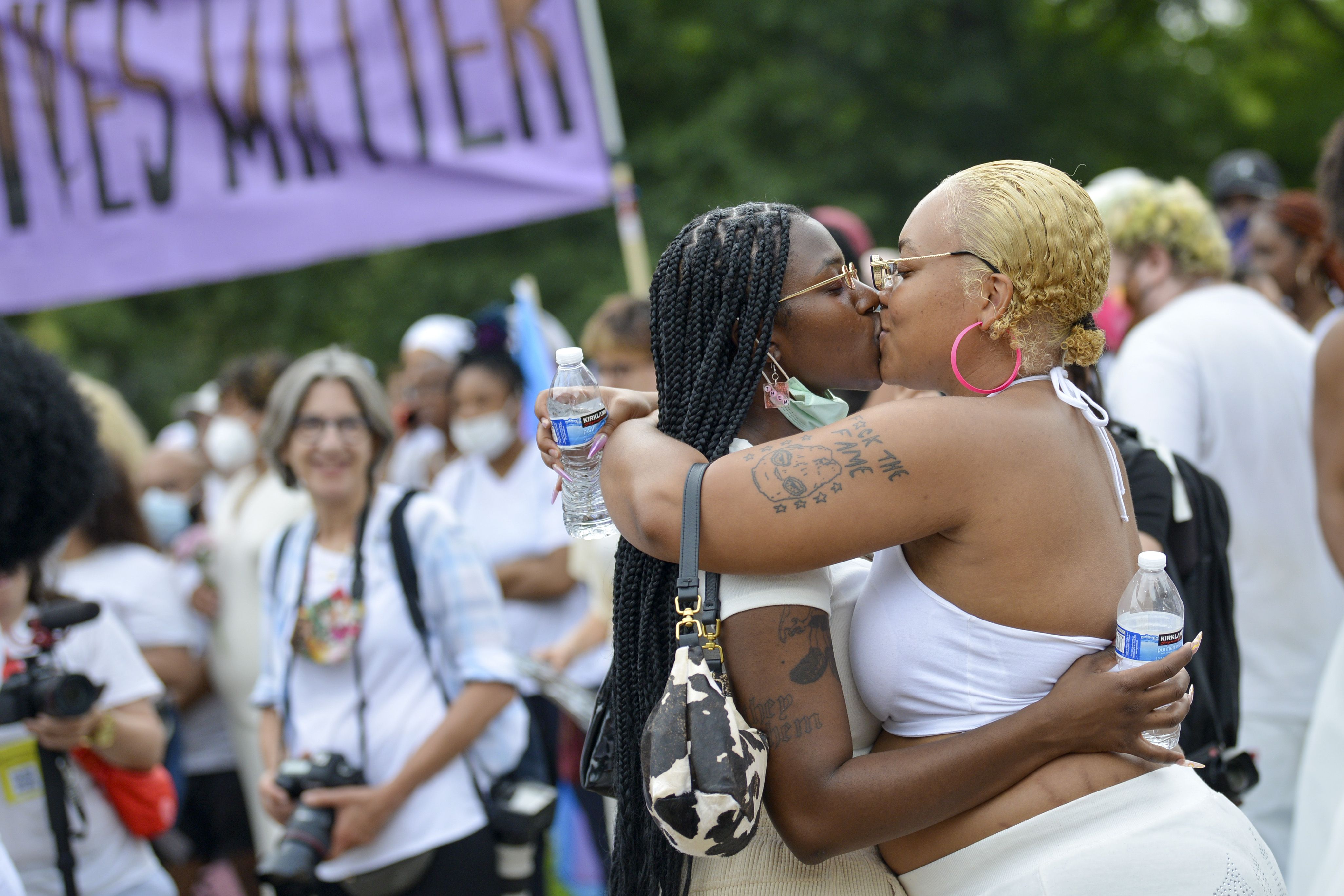 Photo of two women kissing amid a crowd of people rallying for Pride and trans youth
