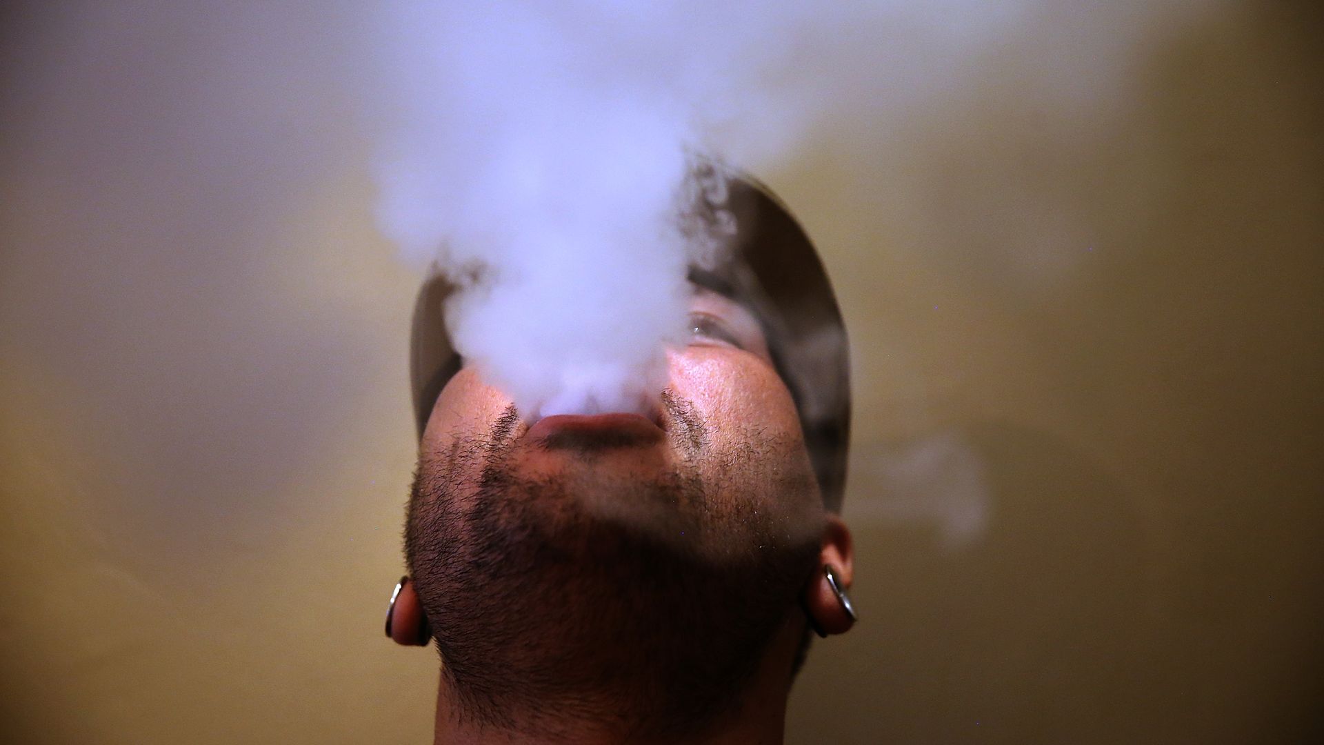 Man blowing vaping smoke up into the air above him