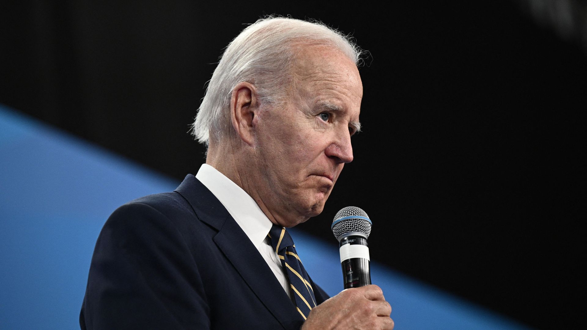 President Joe Biden holds a mic to his face as he speak.