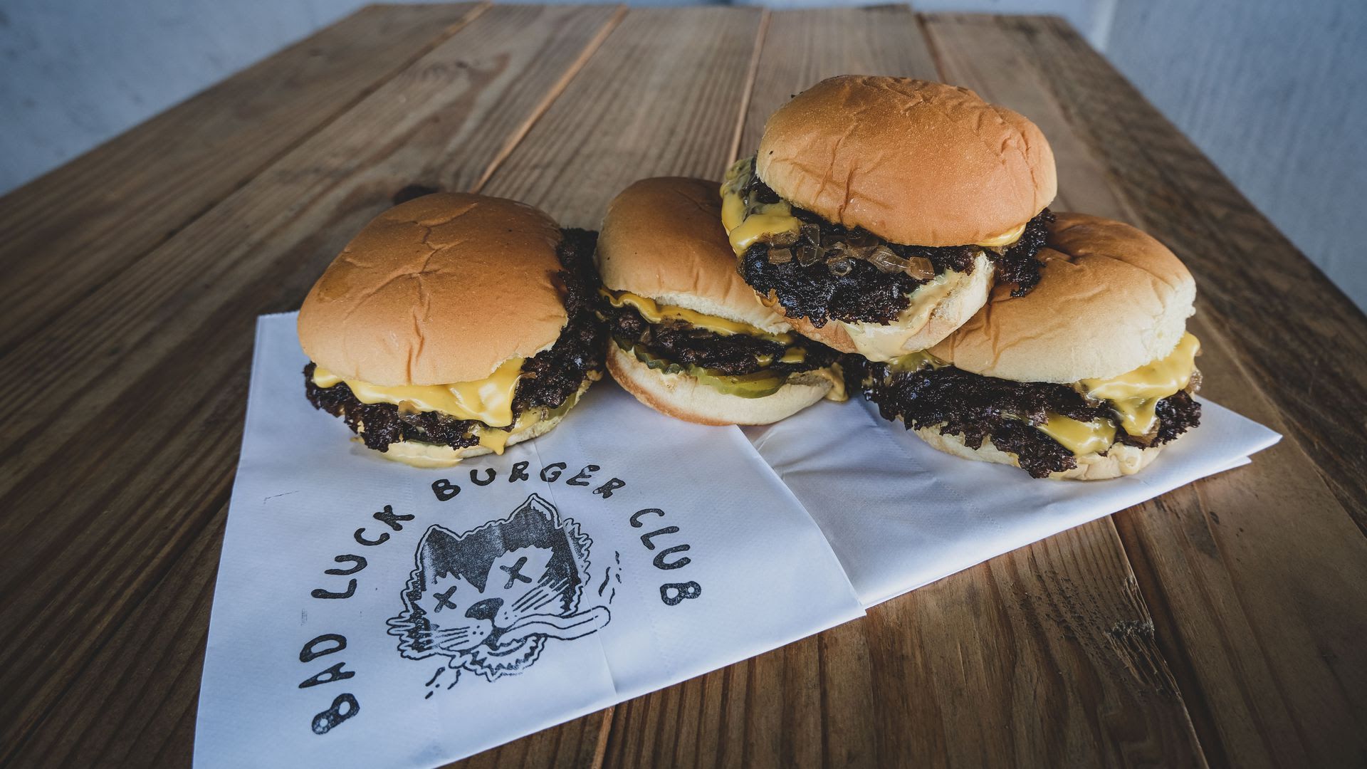 Four Bad Luck Burger Club burgers sit on a paper napkin