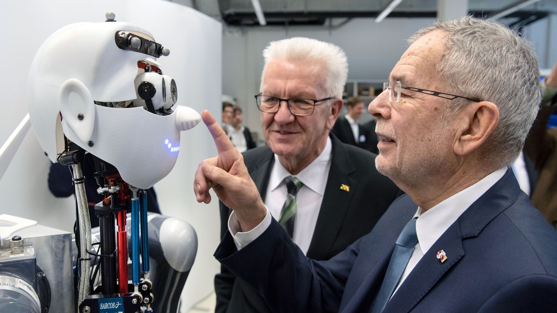 Photo of a man touching a robot’s nose as another man looks on 