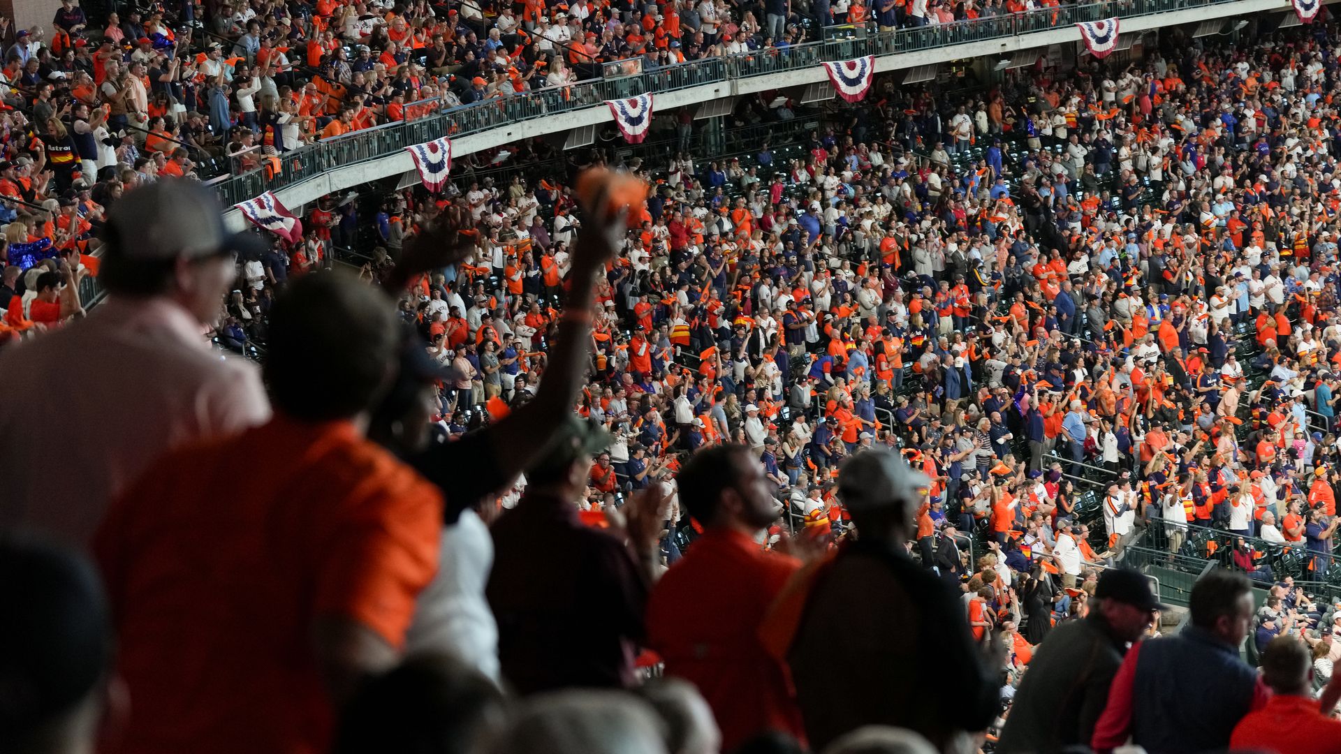 Astros fans wearing orange and white cheer on the team in the stands