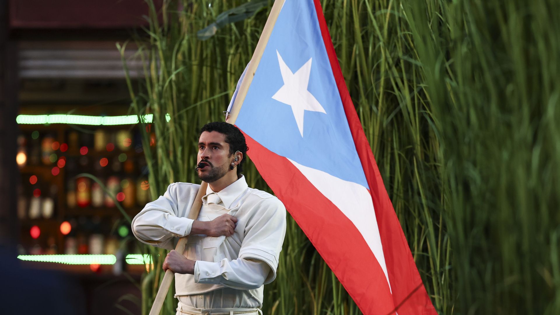 Bad Bunny wearing a white shirt and white pants performance outfit while holding the Puerto Rico flag