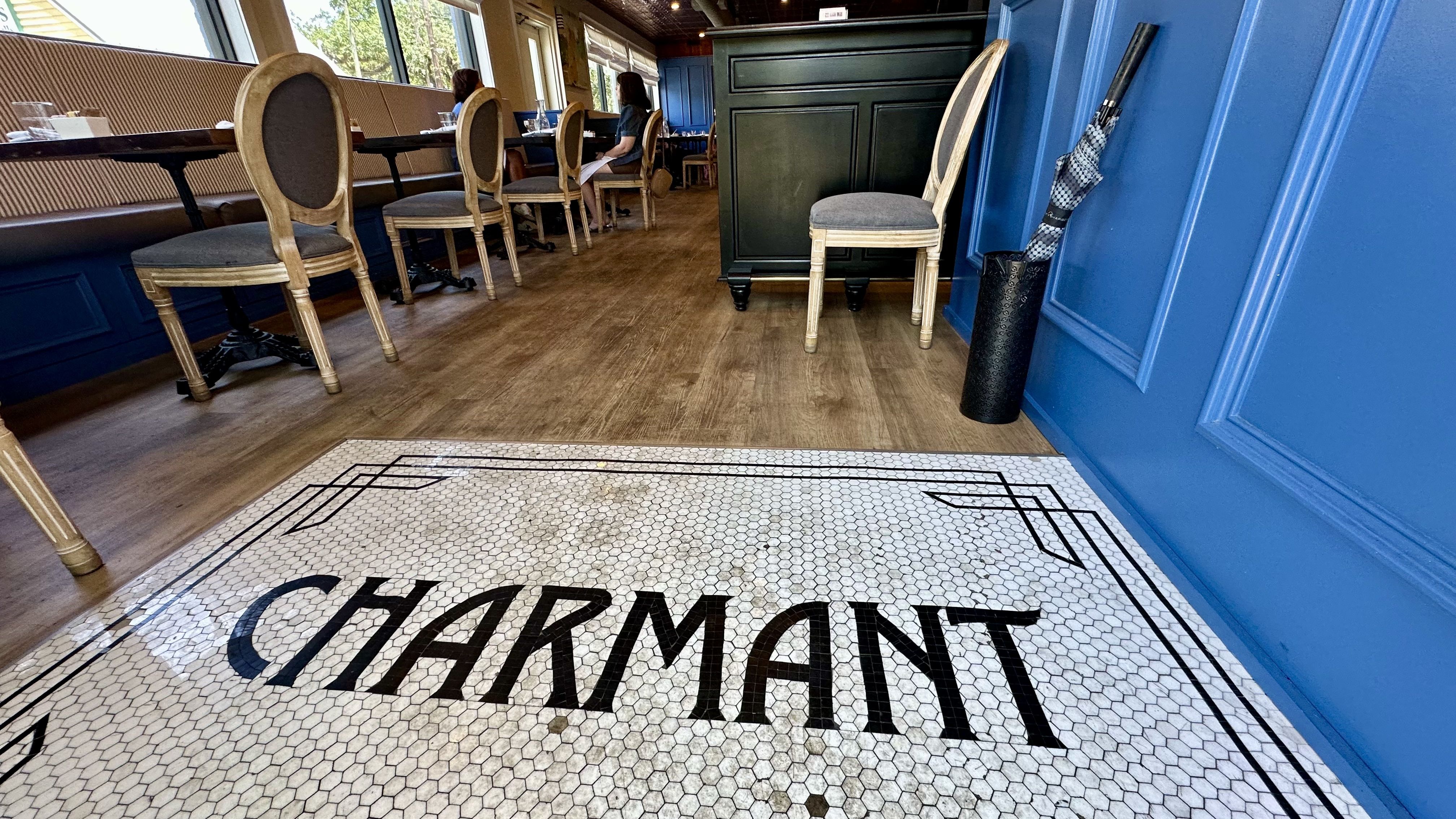 Image shows "Charmant" written in tile on the floor of a restaurant dining room.