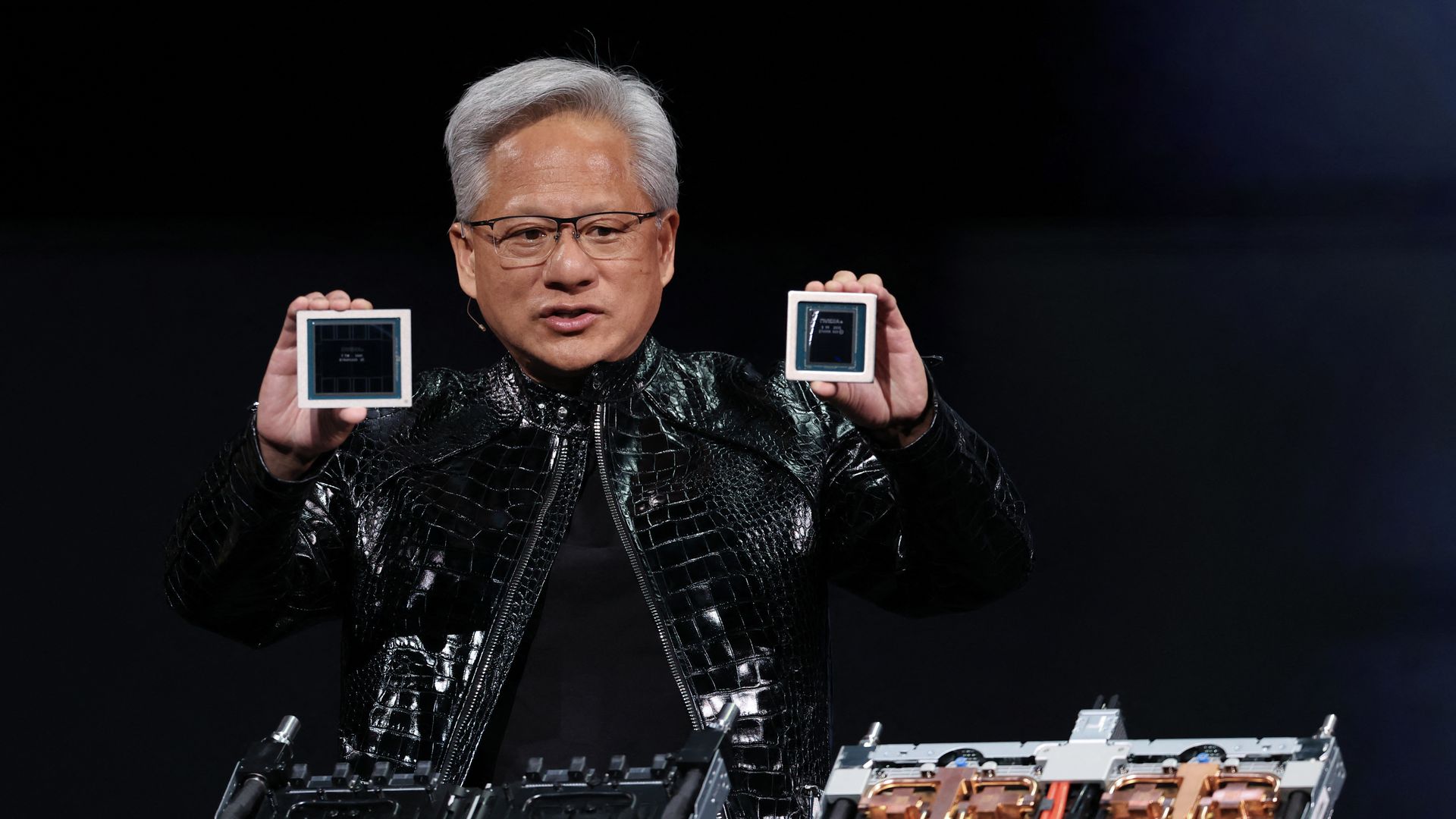Nvidia CEO Jensen Huang, on a stage in a black leather jacket, holding two computer chips in his hands.