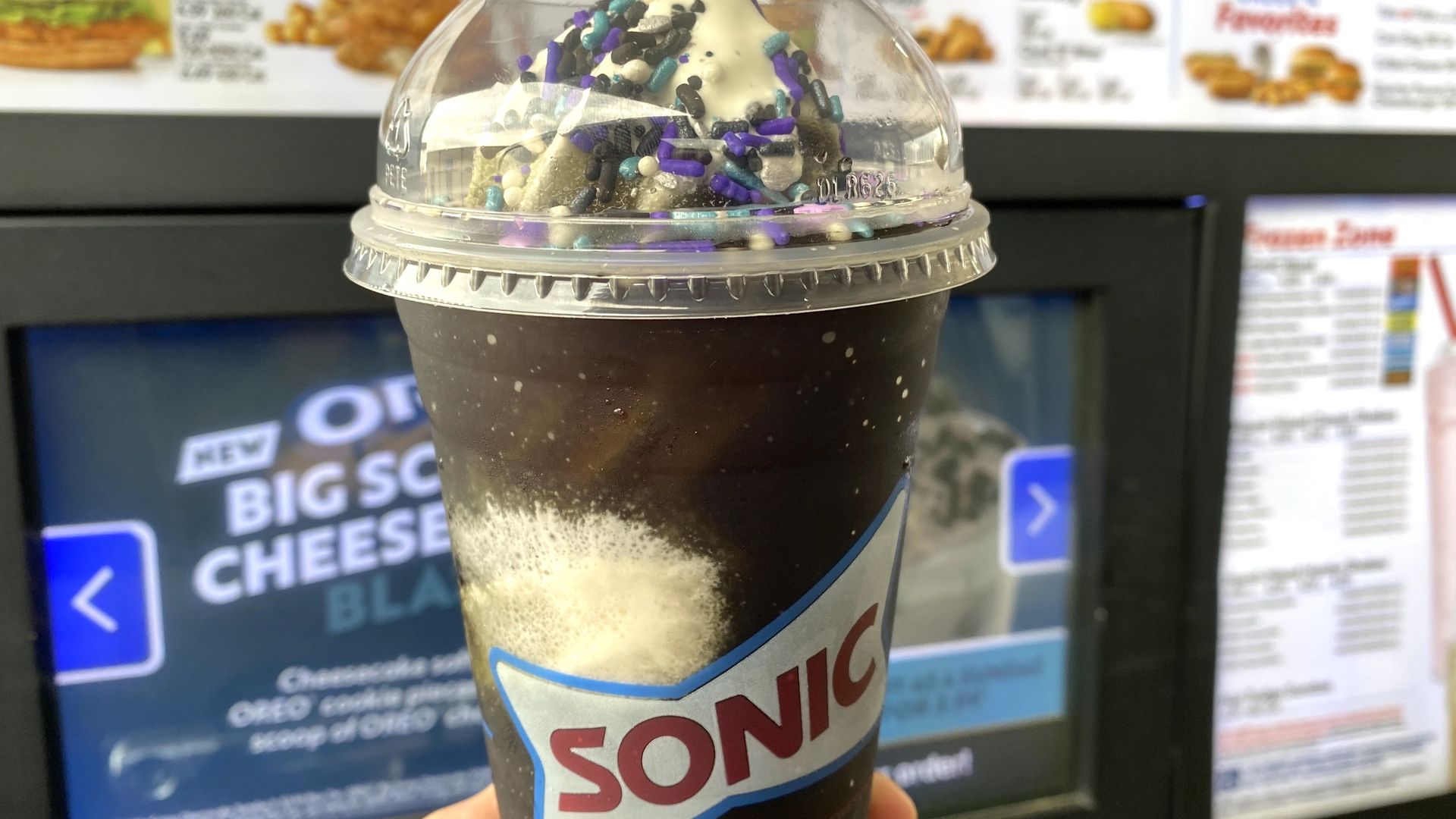 Photo of a Sonic Blackout Slush Float being held in front of a Sonic menu. 