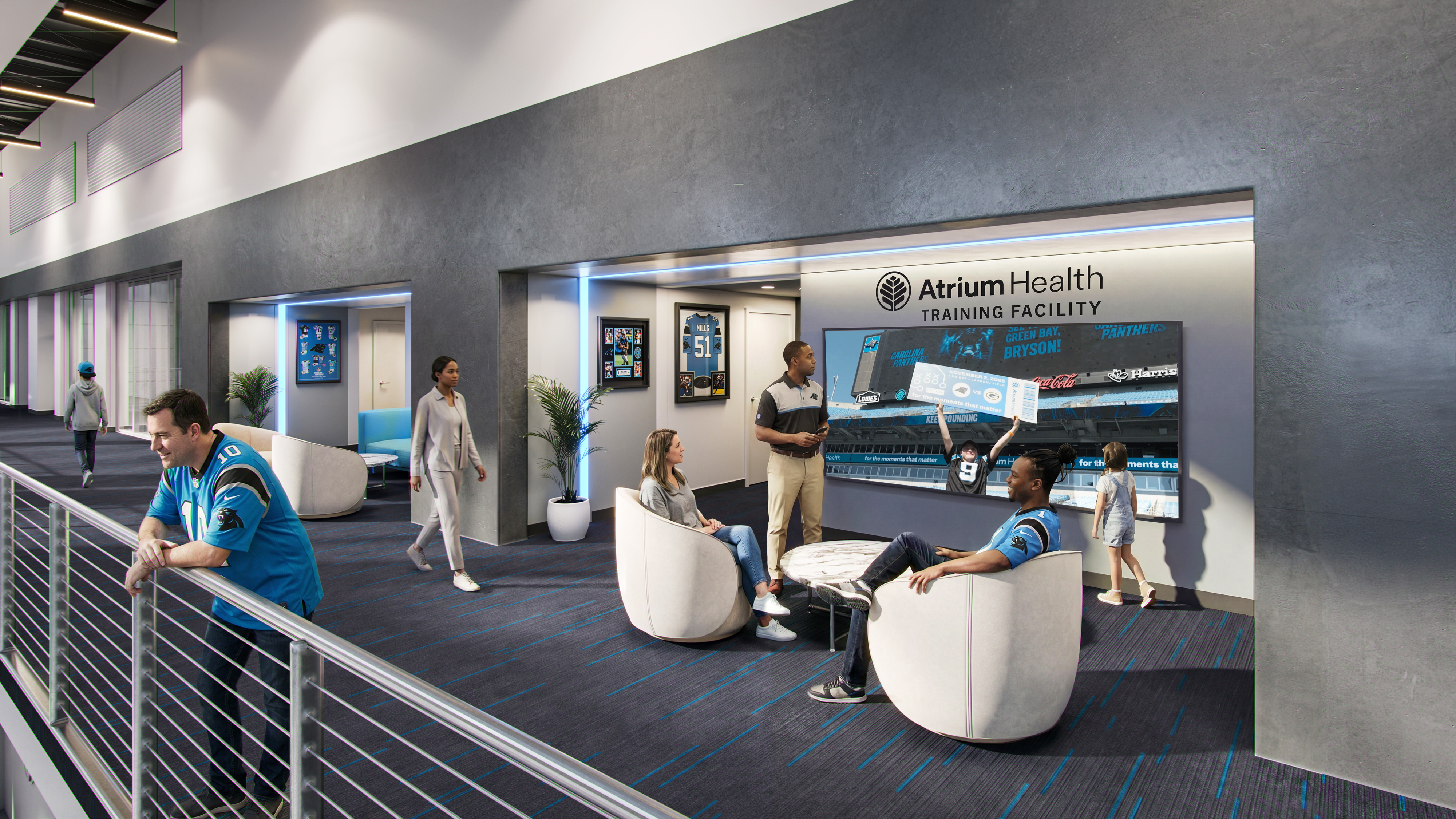 Lobby scene at Atrium Health Training Facility: grey walls, blue lighting, and a large wall screen with the facility name. People sit and chat in white curved chairs while a staff member talks.