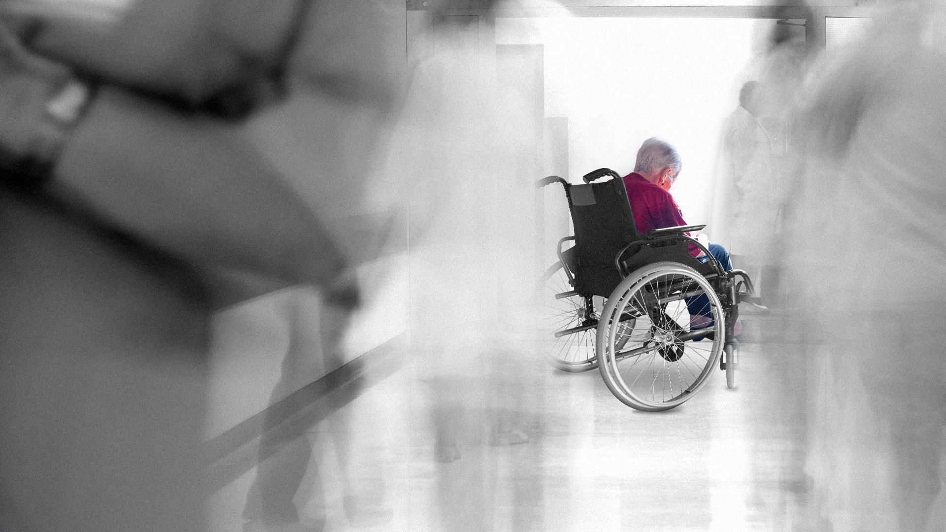Illustration of an elderly woman in a wheelchair surrounded by blurry nursing staff.