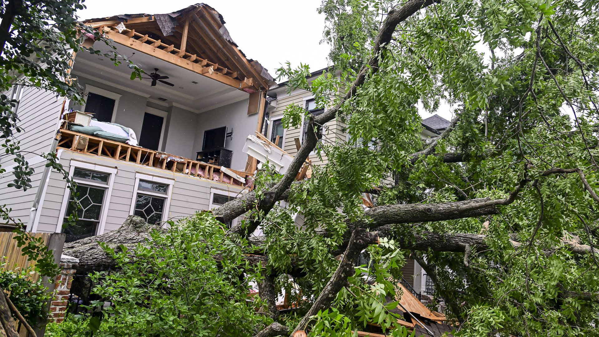 Photo of a tree uprooted and damaged roof and second floor of a home in Houston after severe storms hit.