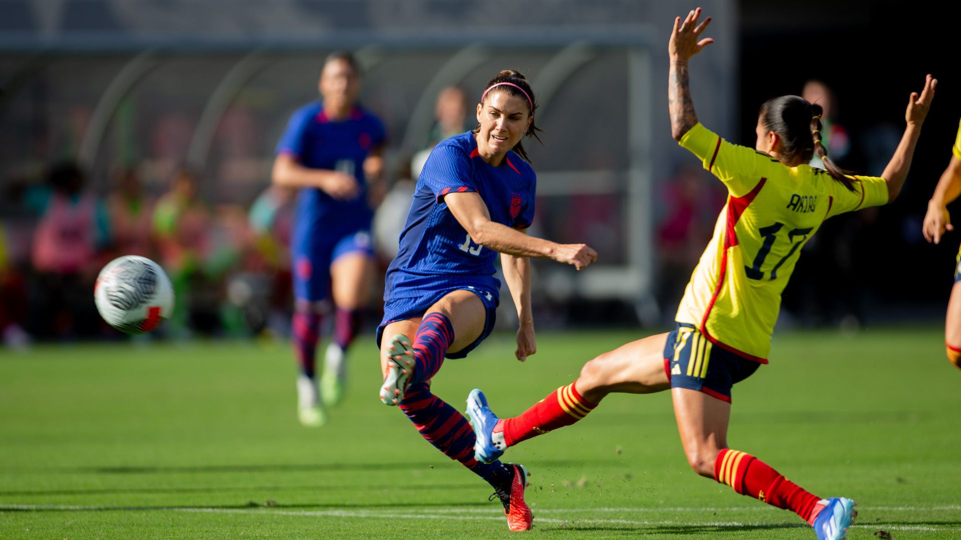 Soccer player Alex Morgan takes a shot past a defender in a game. 