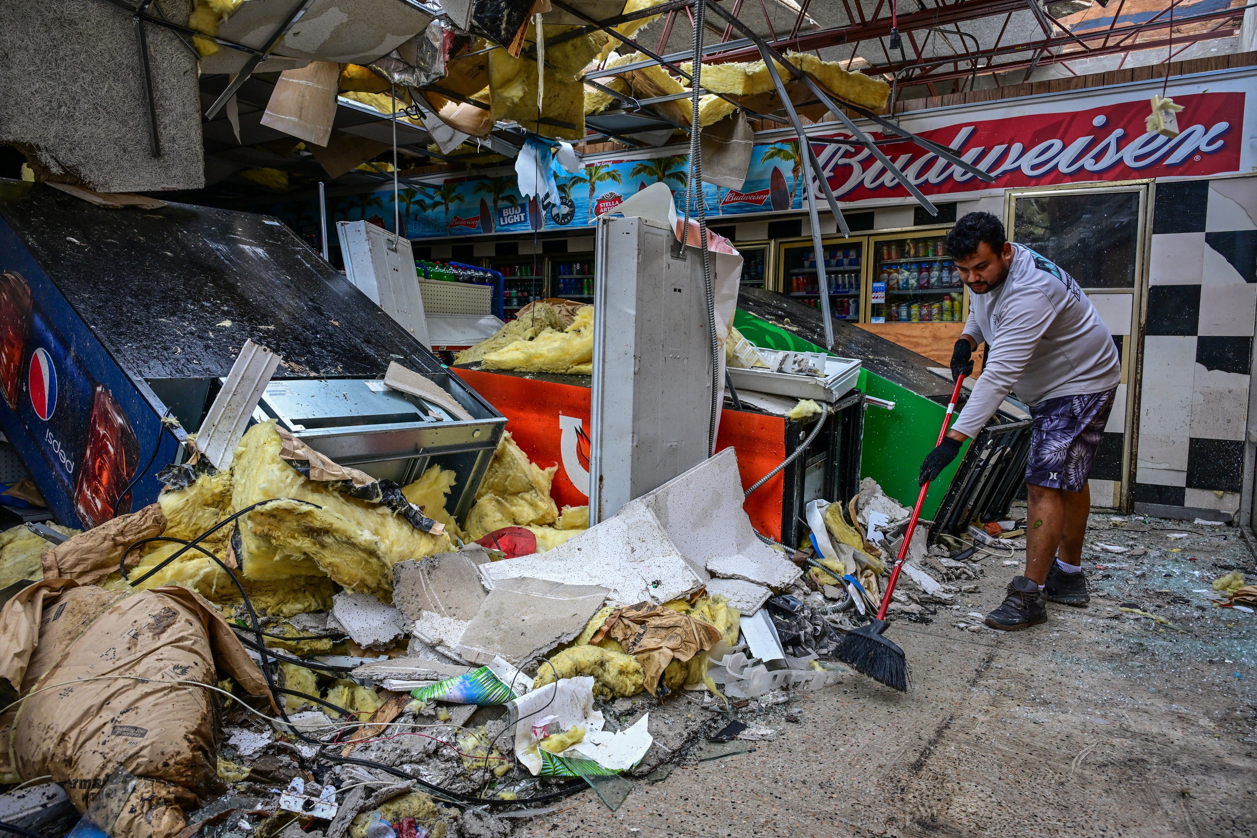 TOPSHOT - A man cleans debris inside a gas station store in Lakewood Park, Florida, after a tornado hit the area and caused severe damage as Hurricane Milton swept through Florida on October 10, 2024. At least 10 people were dead after Hurricane Milton smashed into Florida, US authorities said, afte