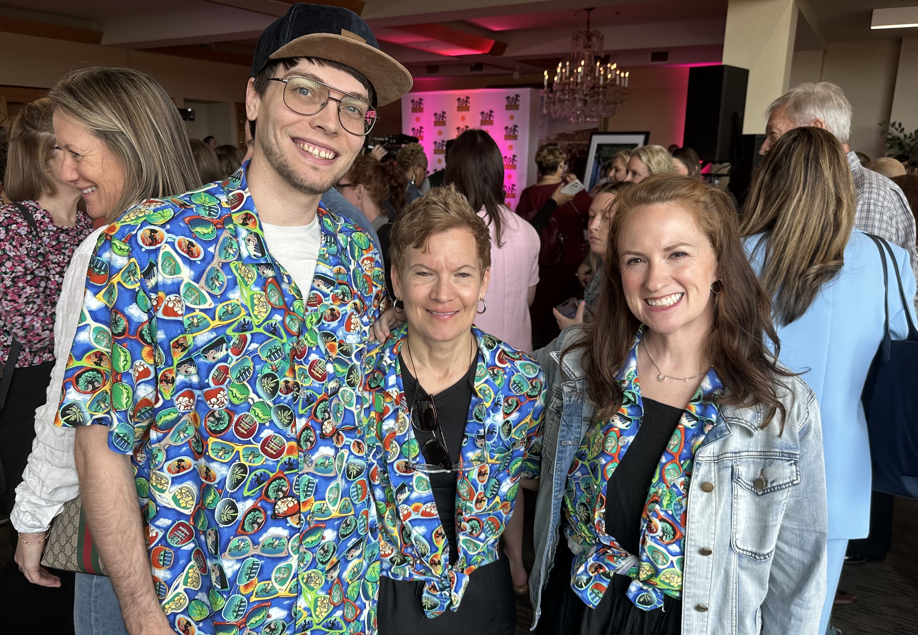 Three people, wearing Bayouwear shirts with an illustrated pattern of sunglasses, smile in a posed photo.