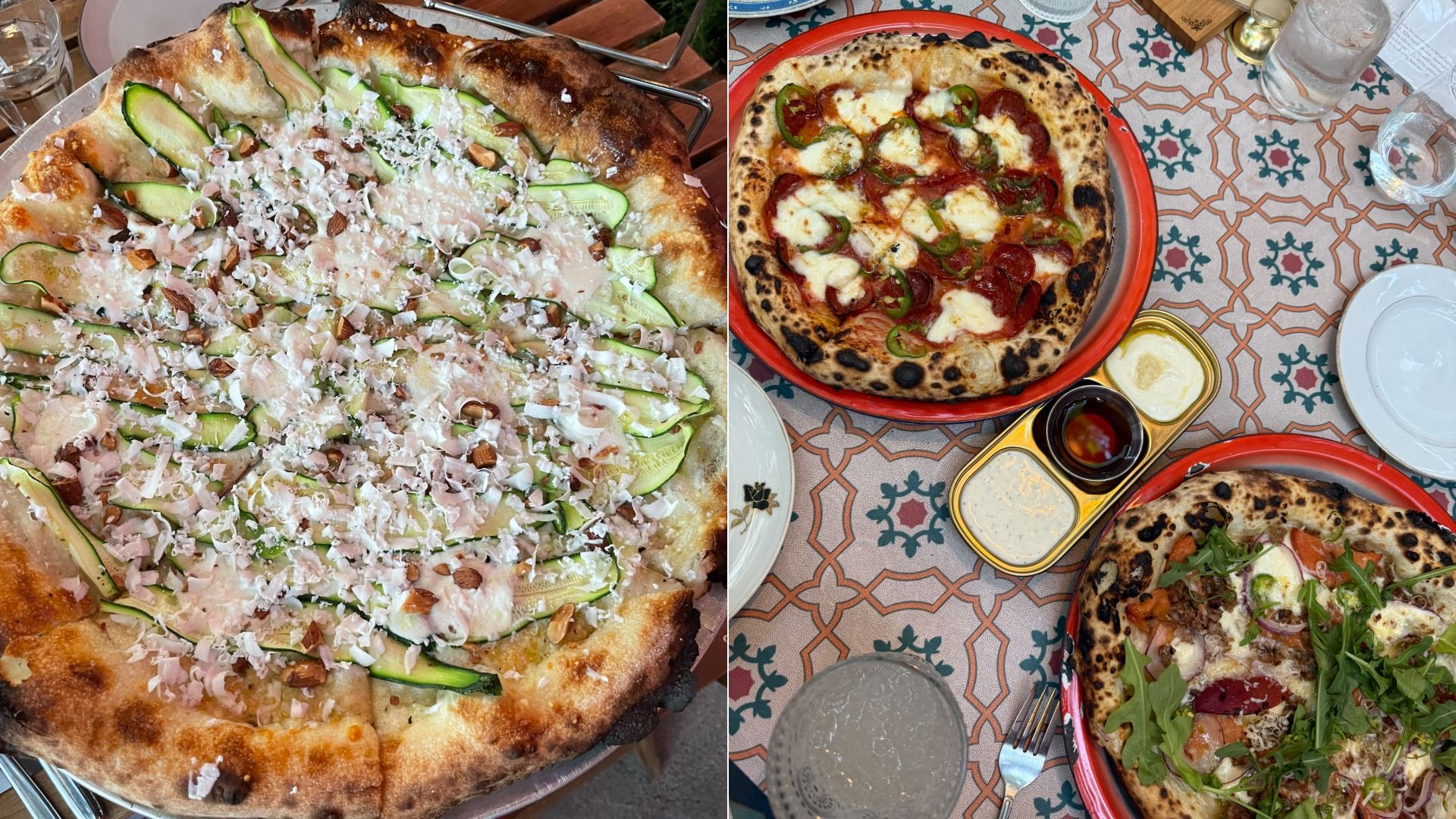 Three artisan pizzas on a patterned tablecloth: one with sliced zucchini, cheese, and nuts; one with pepperoni, melted cheese, and green peppers; one with arugula, tomatoes, onions, and cheese. Four glasses and condiments on the table.
