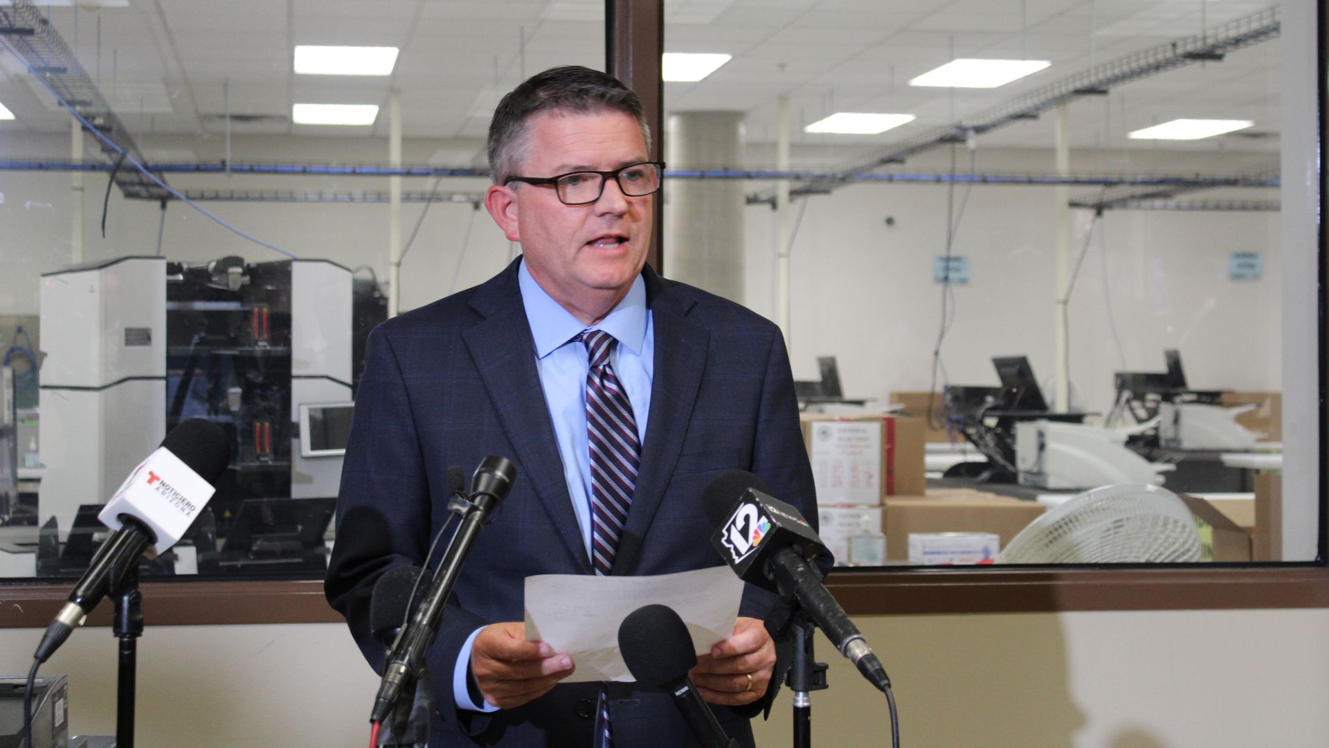 Maricopa County Board of Supervisors Chairman Bill Gates stand in front of microphones while reading from a piece of paper