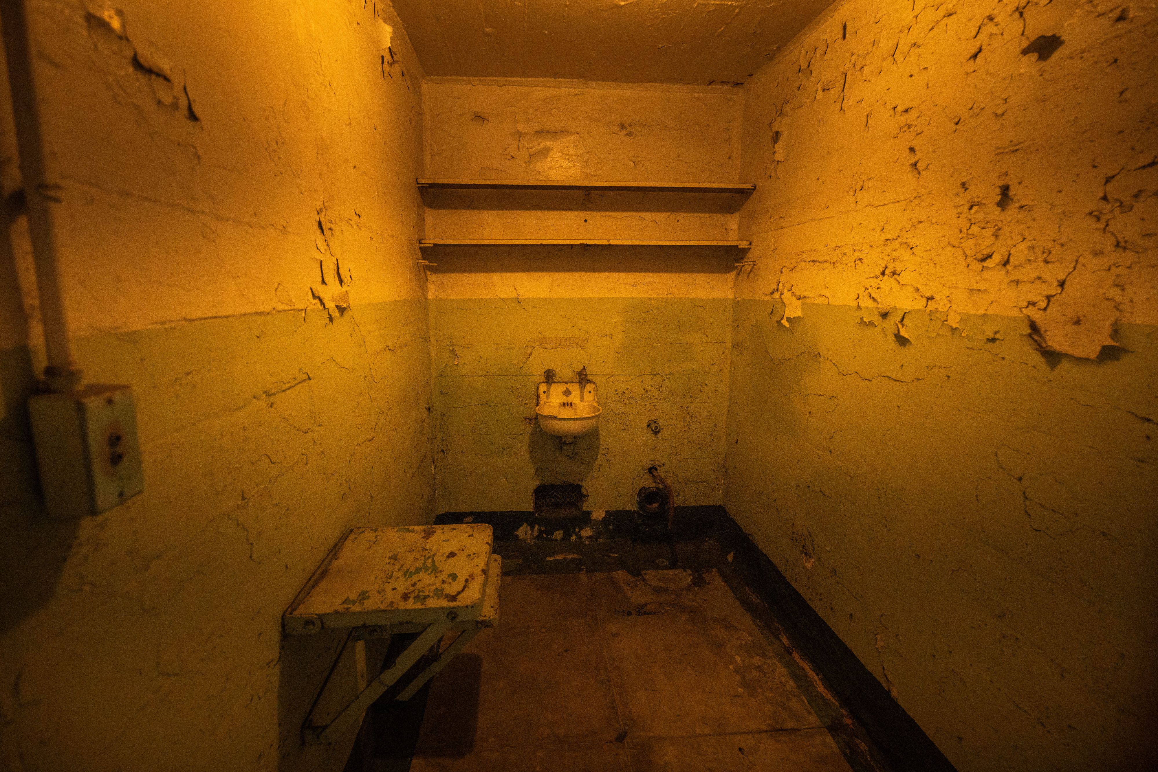 Photo of a crumbling cell featuring a narrow space, sink and bench