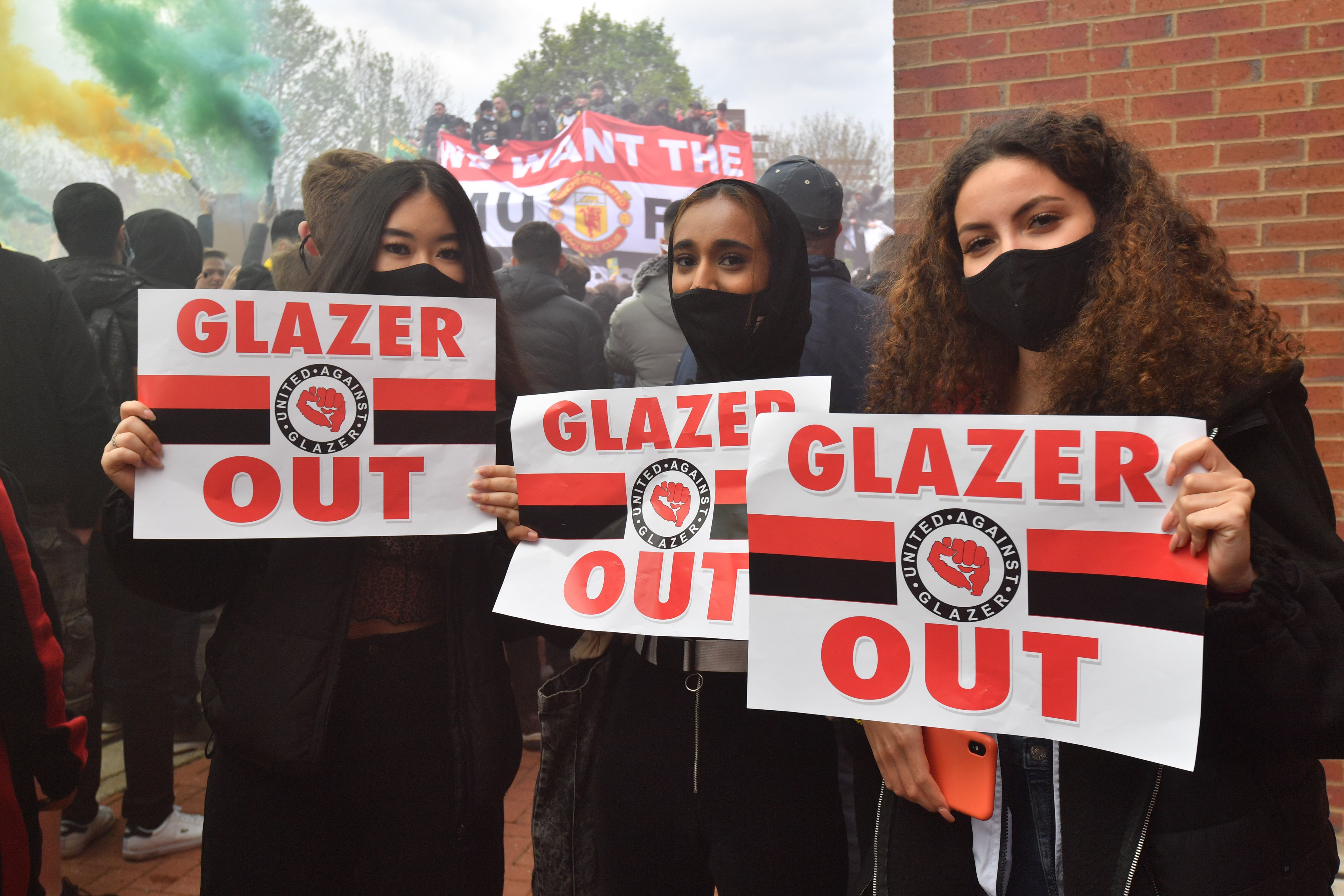 Three women hold signs that read "Glazer Out" 