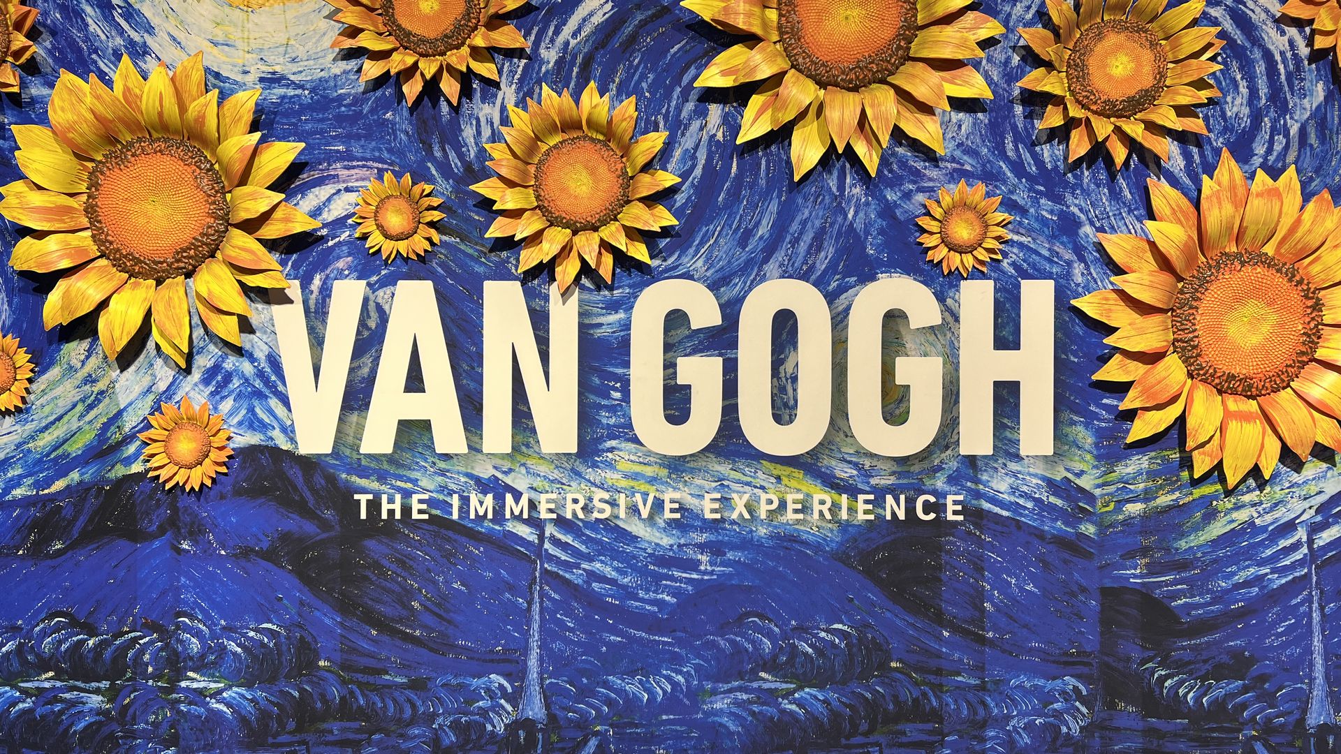 a rendition of van gogh's starry nights with large sunflowers surrounding words that say "VAN GOGH the immersive experience"
