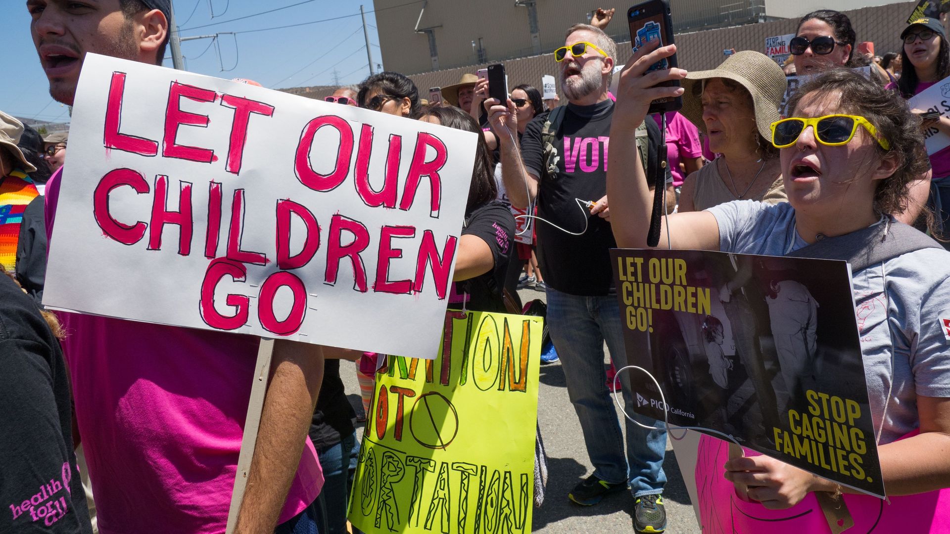 Protestors in a crowd with a man in the fore front holding a sign that says "let our children go"