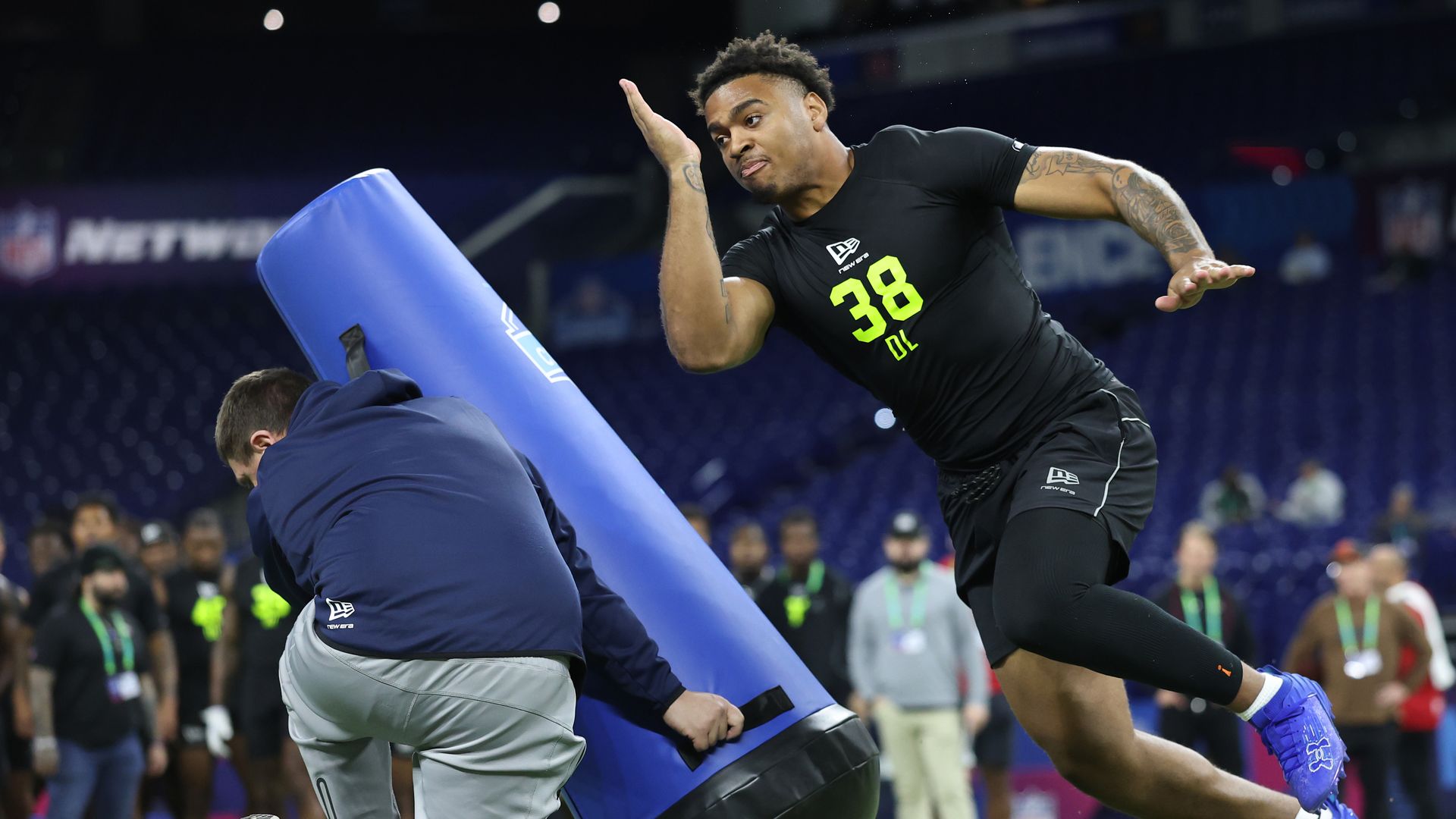 Keldric Faulk, wearing black shorts and a black t-shirt with the number 38 on it, participates in a drill as a trainer holds an obstacle and Faulk avoids it.