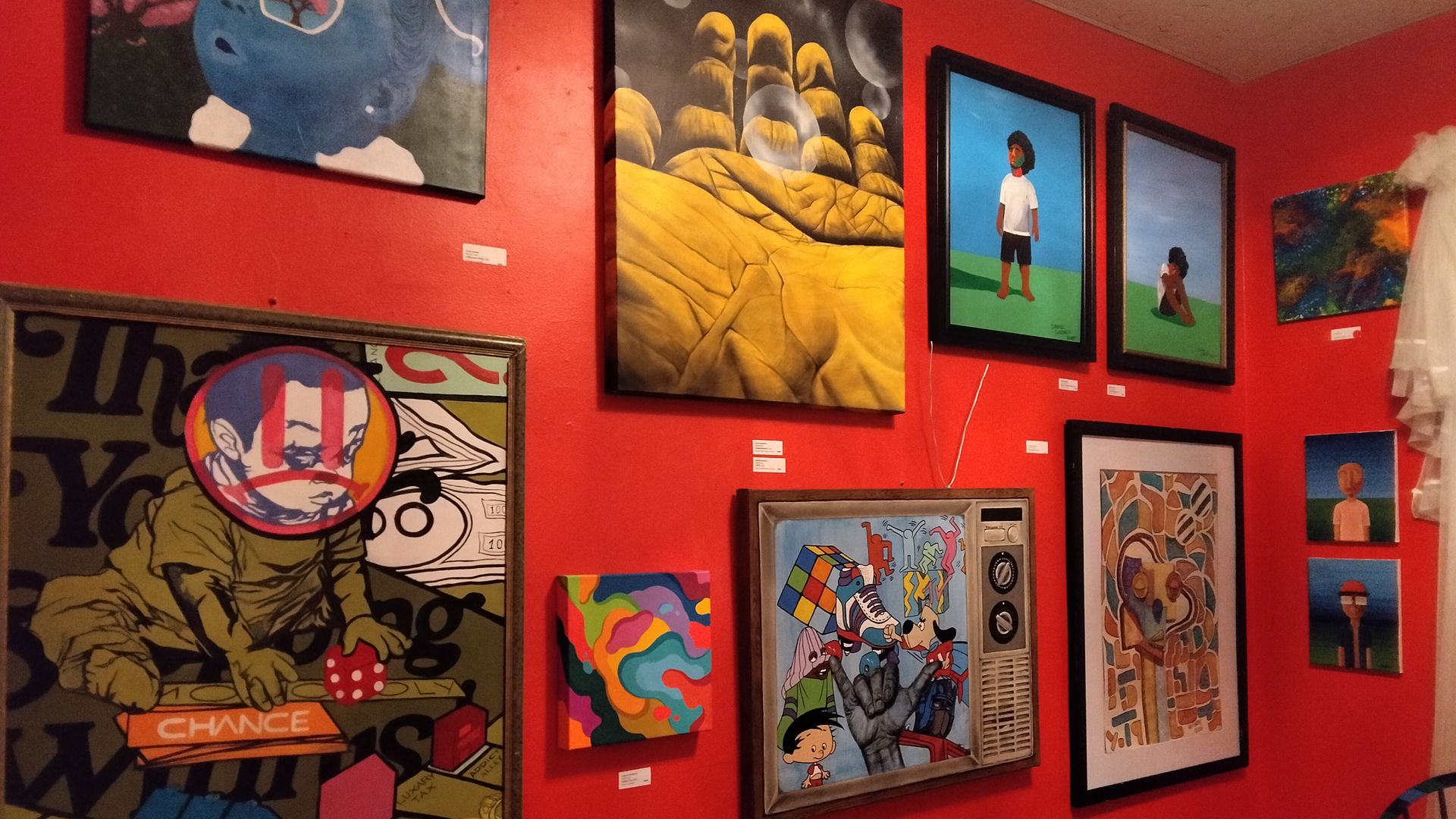 Gallery wall with various colorful paintings on a red background, including abstract, surreal and cartoon styles.