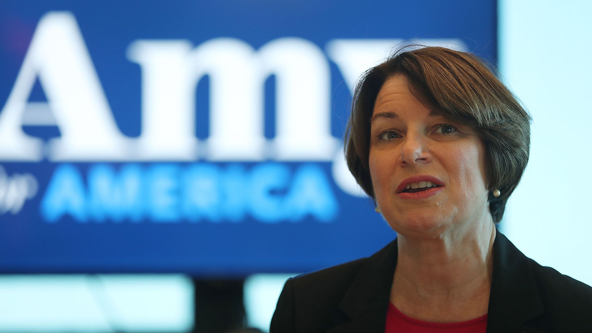 In this image, Amy stands and speaks in front of a sign with her name on it. 