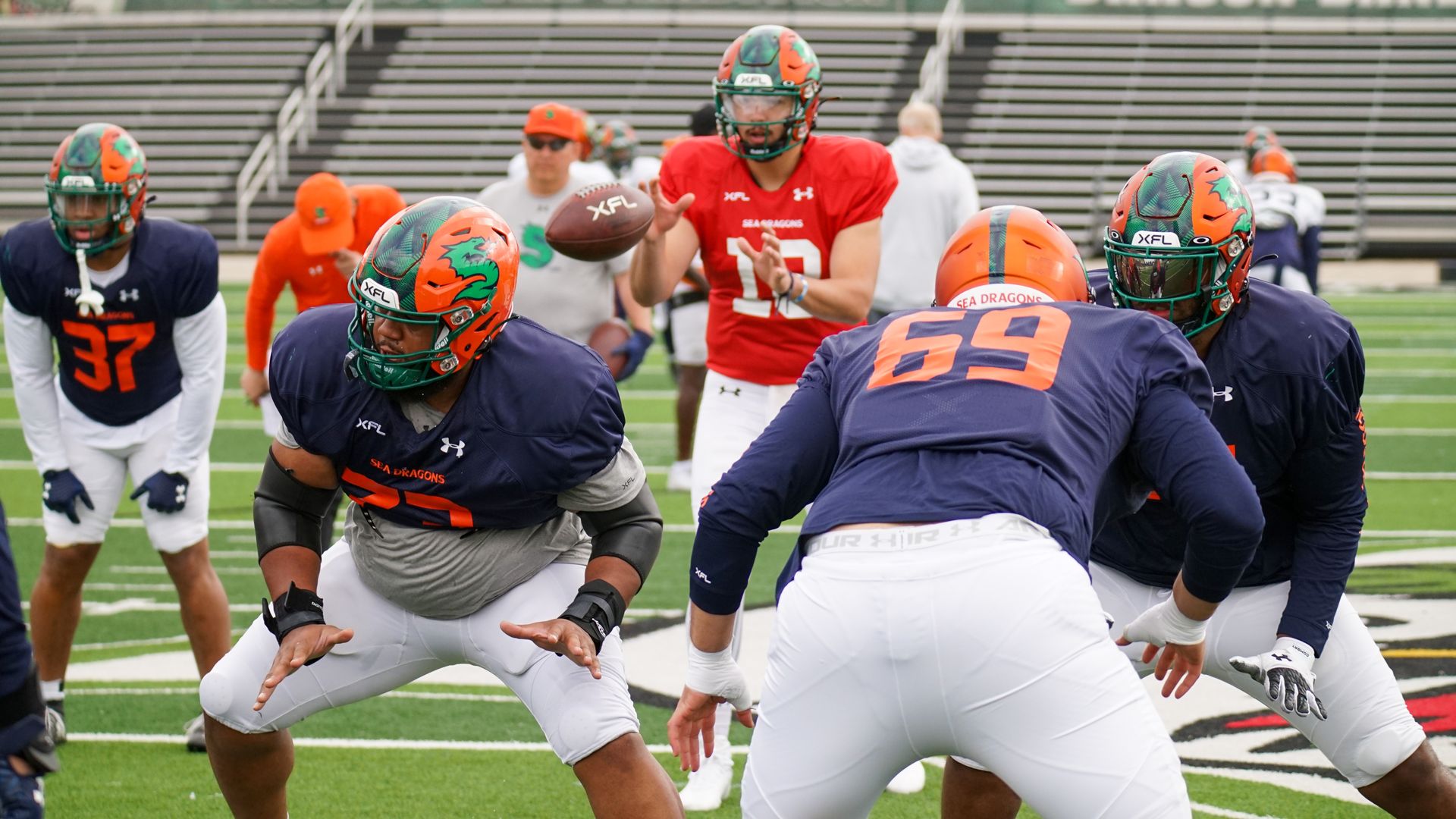 Football players on a field with bleachers in background.