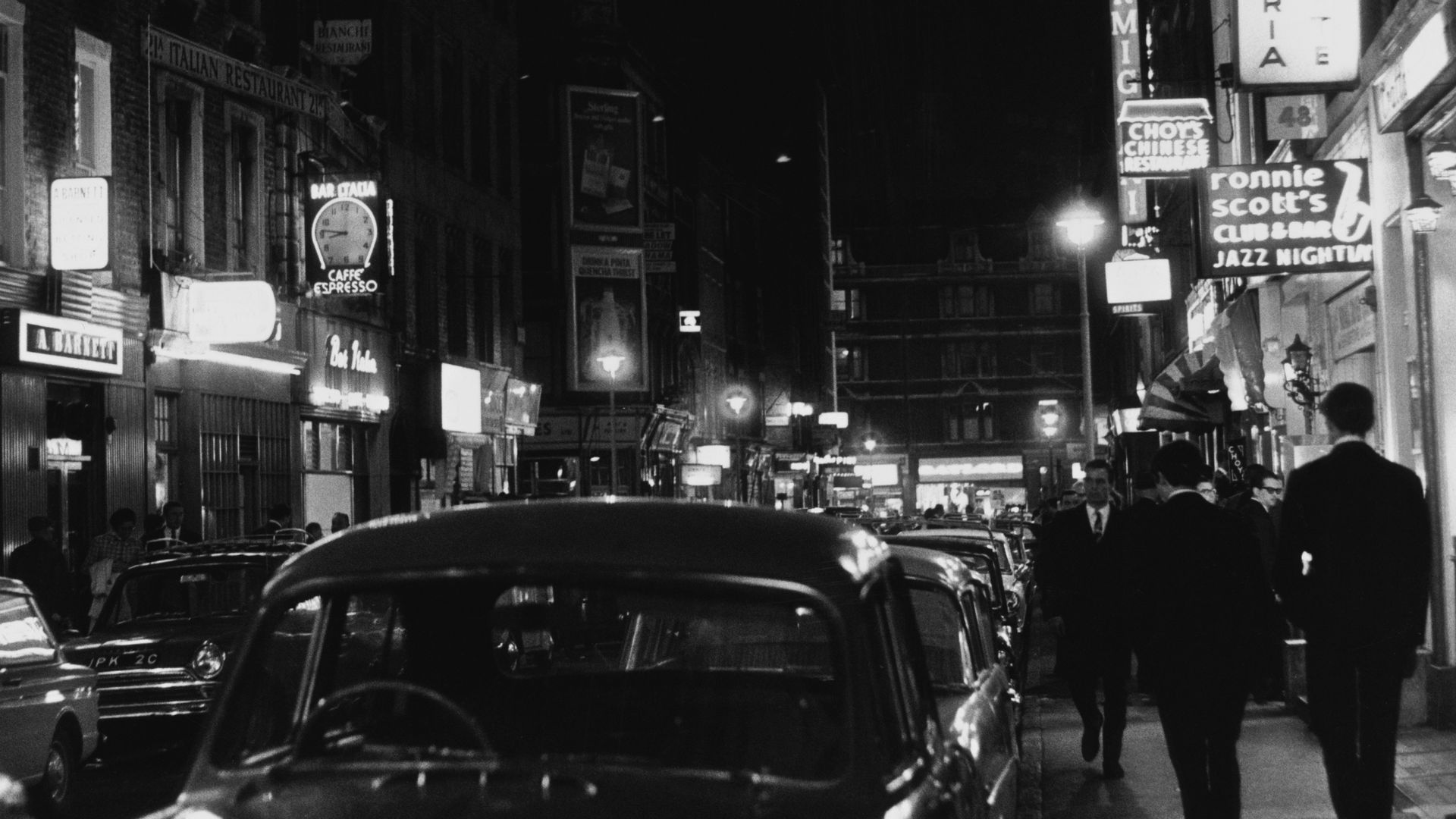 Cars drive down an old street, black and white