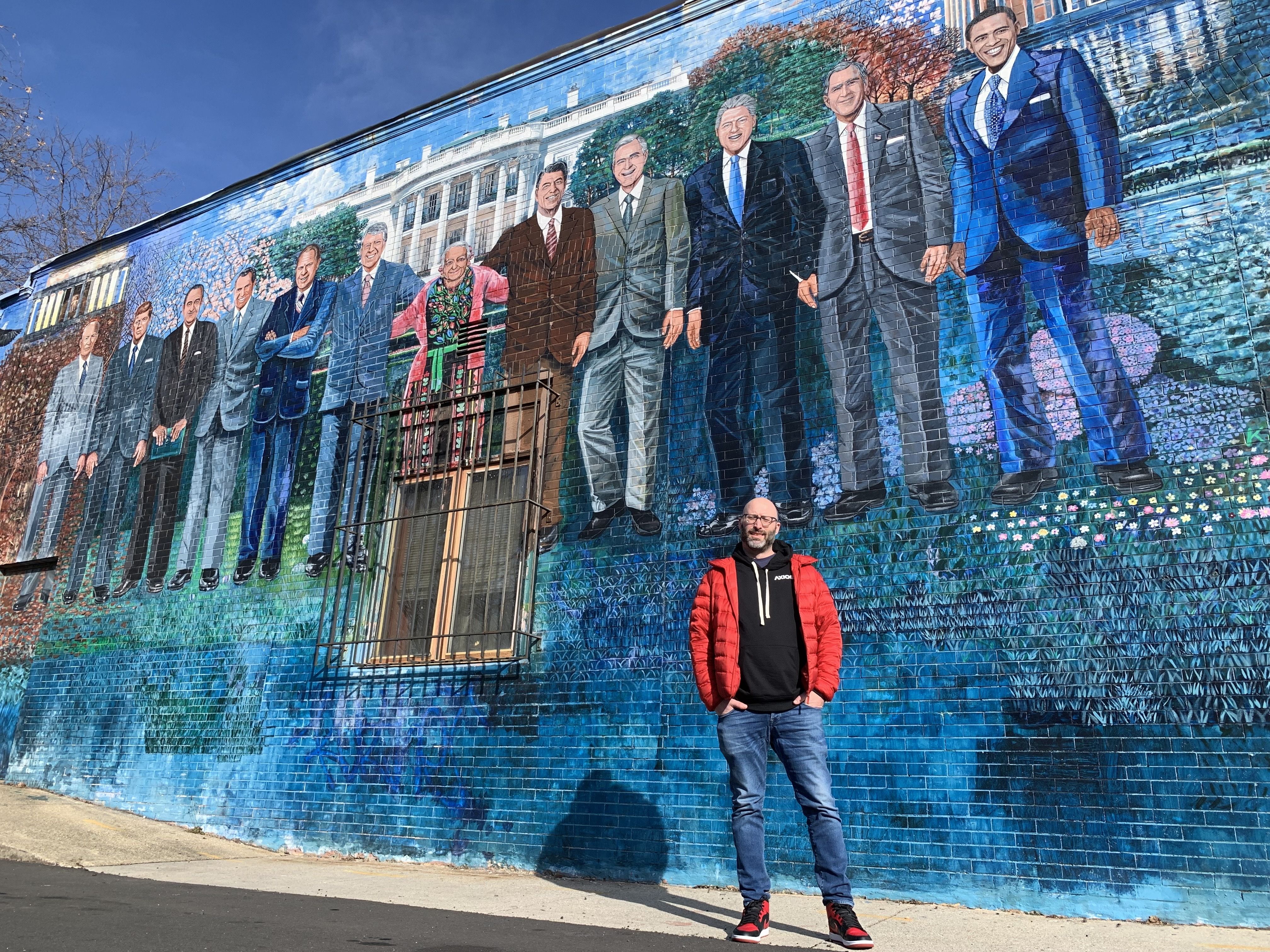 Photo of a man in front of a mural. 