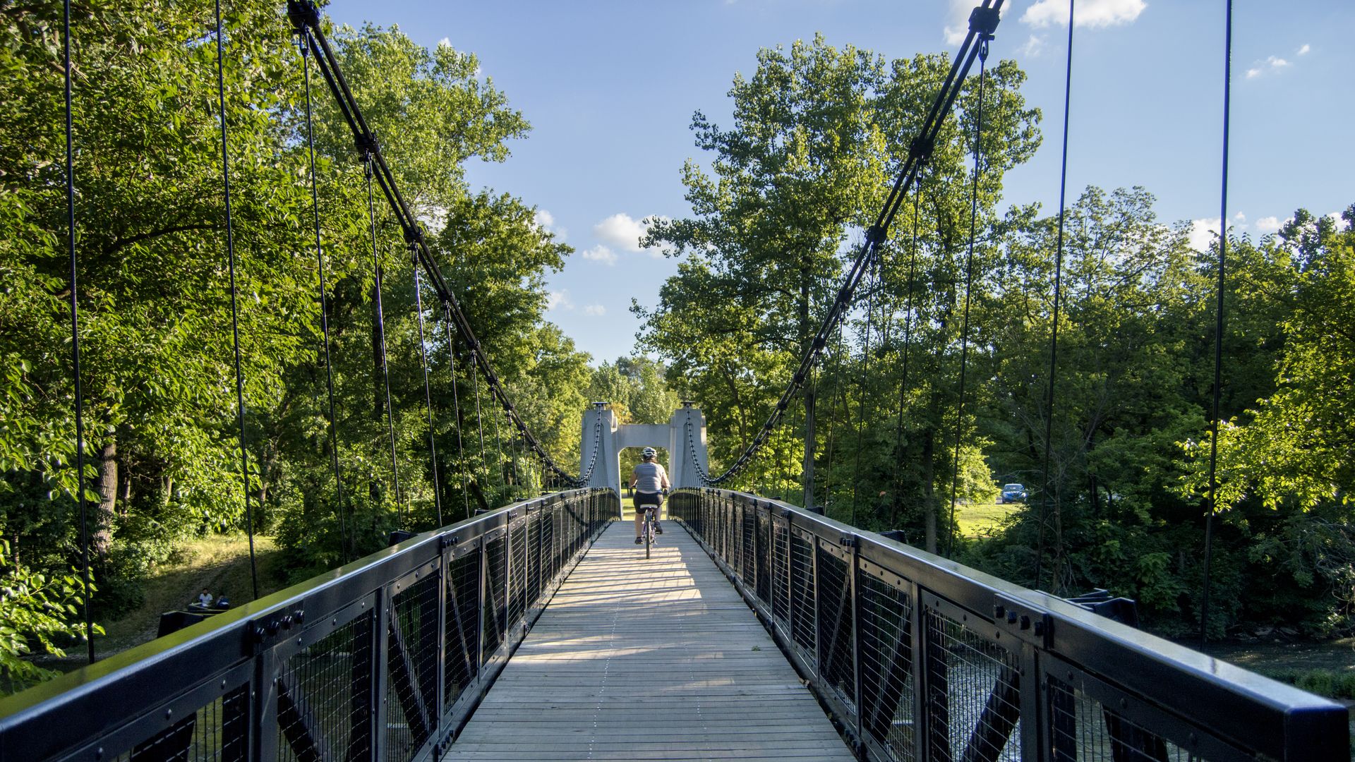 A first-person view on a bridge of the Alum Creek Trail, with a bicyclist and trees in the distance