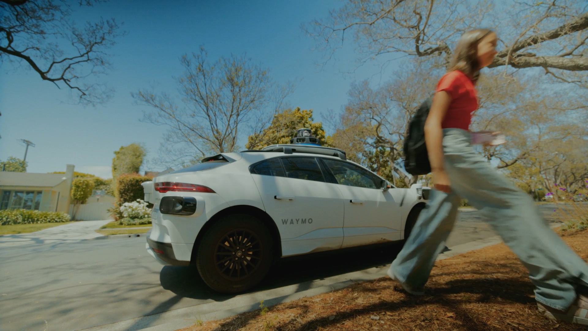 A teenage girl wearing a backpack walks away from a Waymo automated car. 