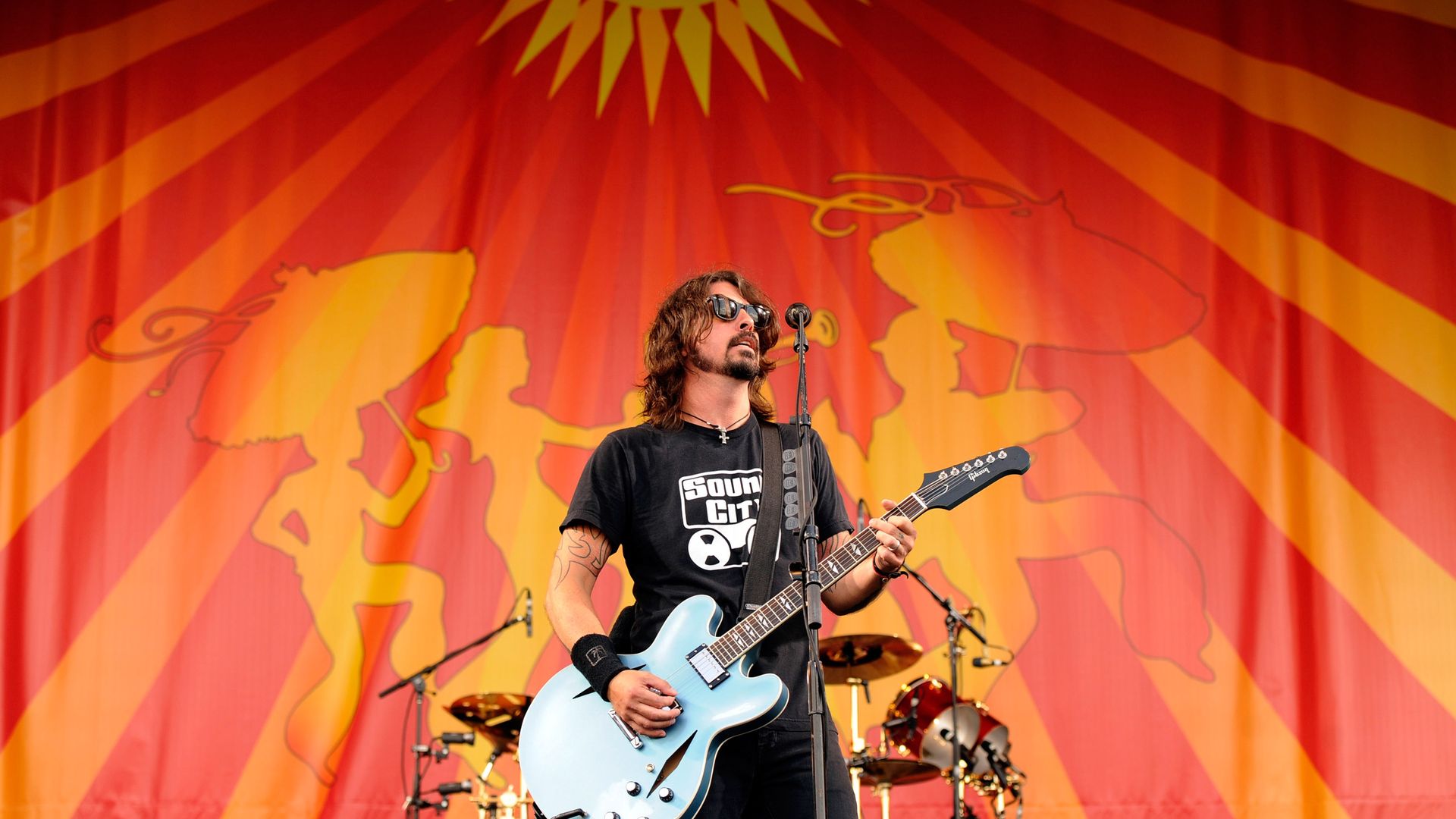Dave Grohl sings into a microphone while playing a guitar at Jazz Fest.