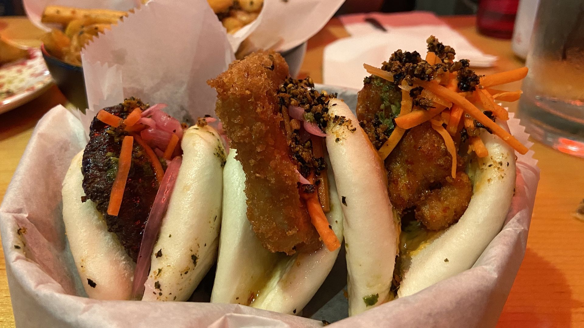 A basket of three bao sandwiches with plant-based “meats” with Tokyo fries in the background