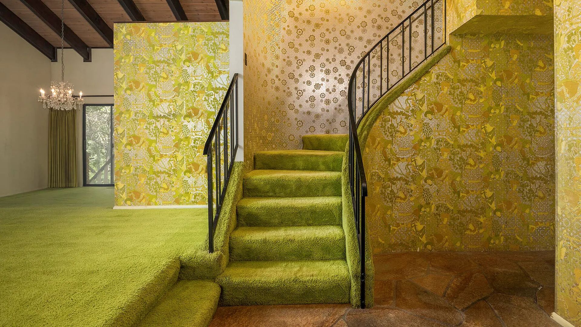A curving staircase with green shag carpet and wrought iron rails swirls over metallic wallpaper depicting medieval scenes.