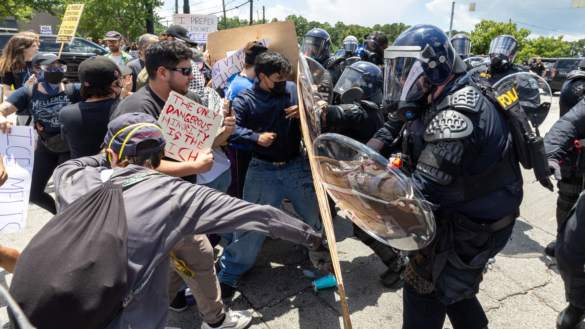 Police in riot gear push back against protesters holding signs at a demonstration in DeKalb County
