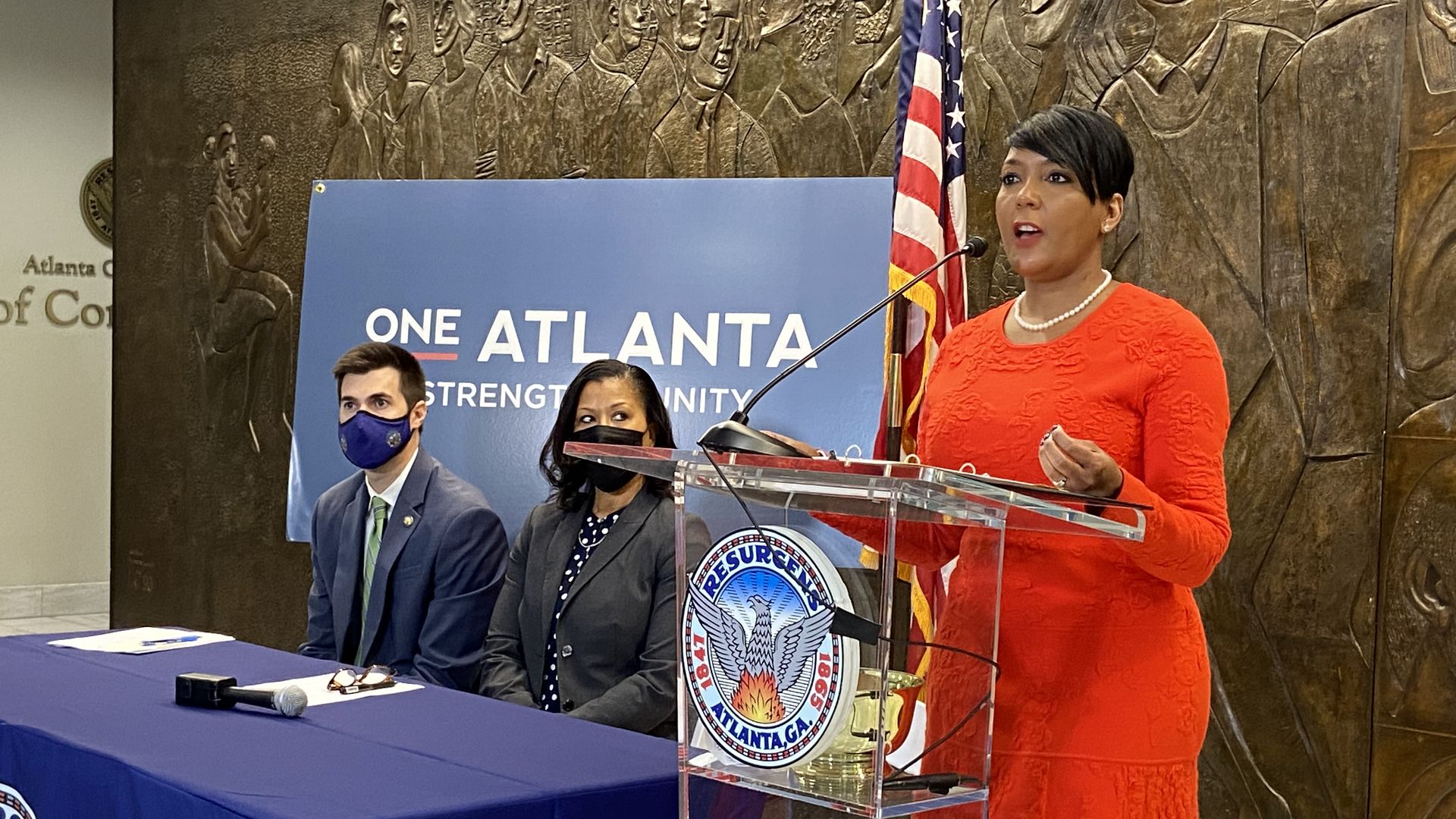 Mayor Keisha Lance Bottoms speaks at a lectern with two staffers seated next to her