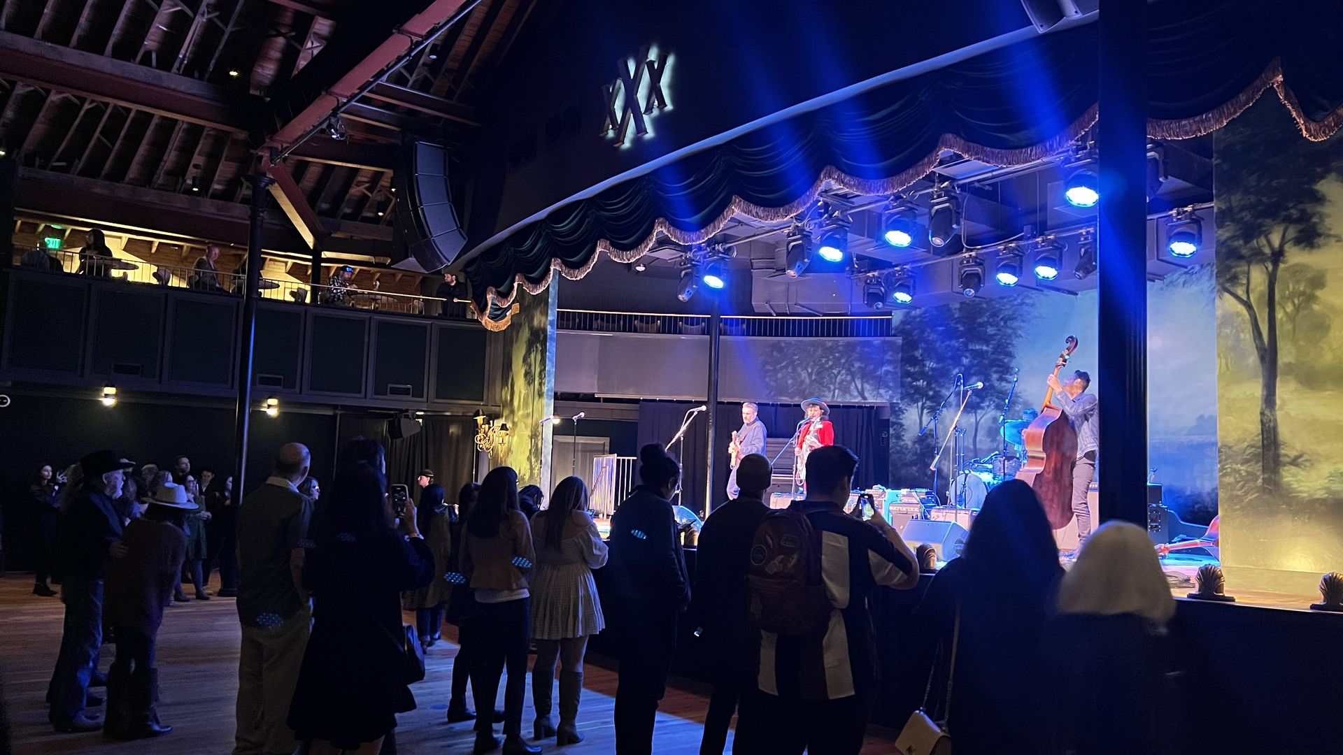 A group of people stands near a stage as a band performs. 