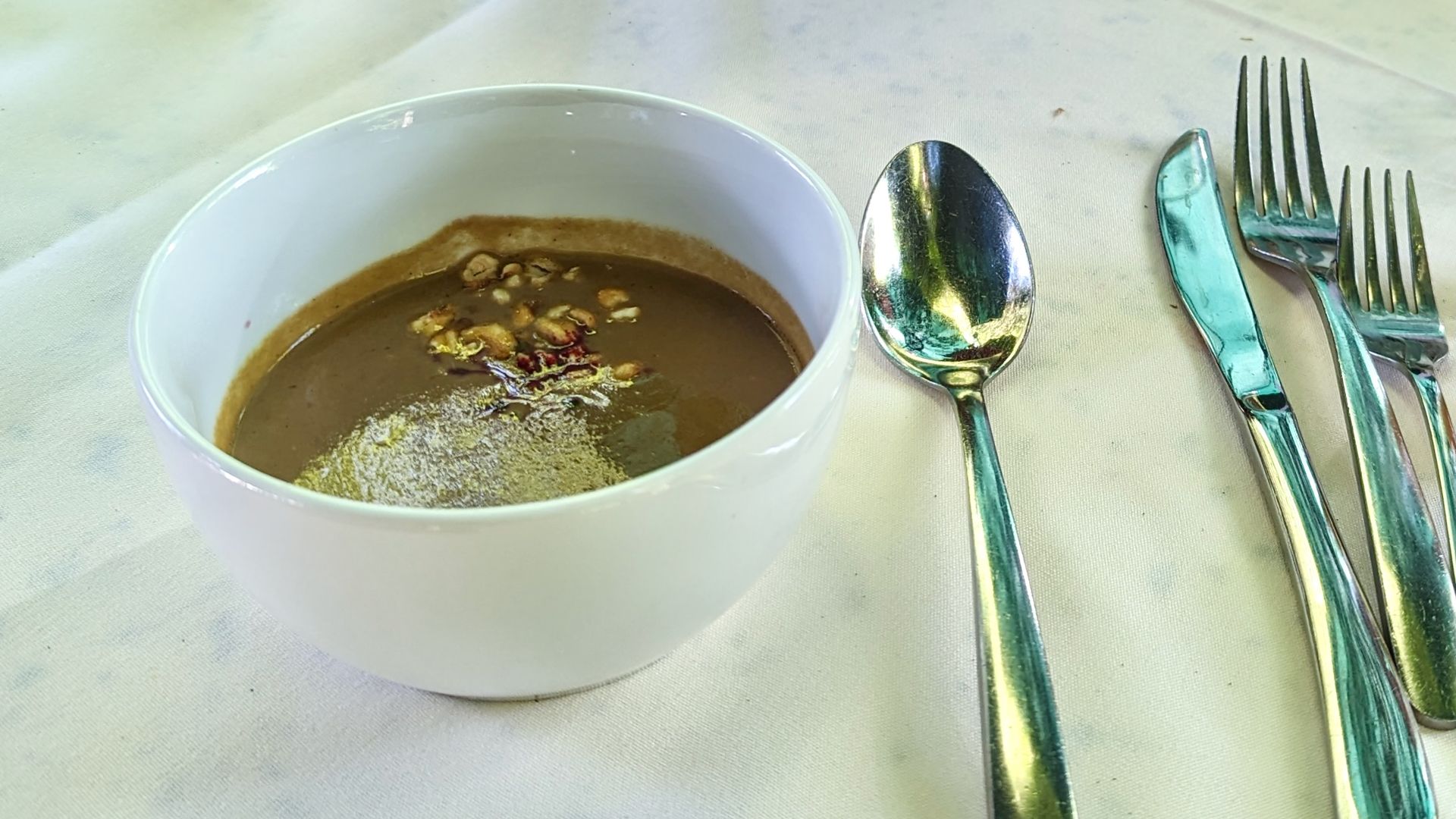 A bowl of brown soup with silverware on a tablecloth