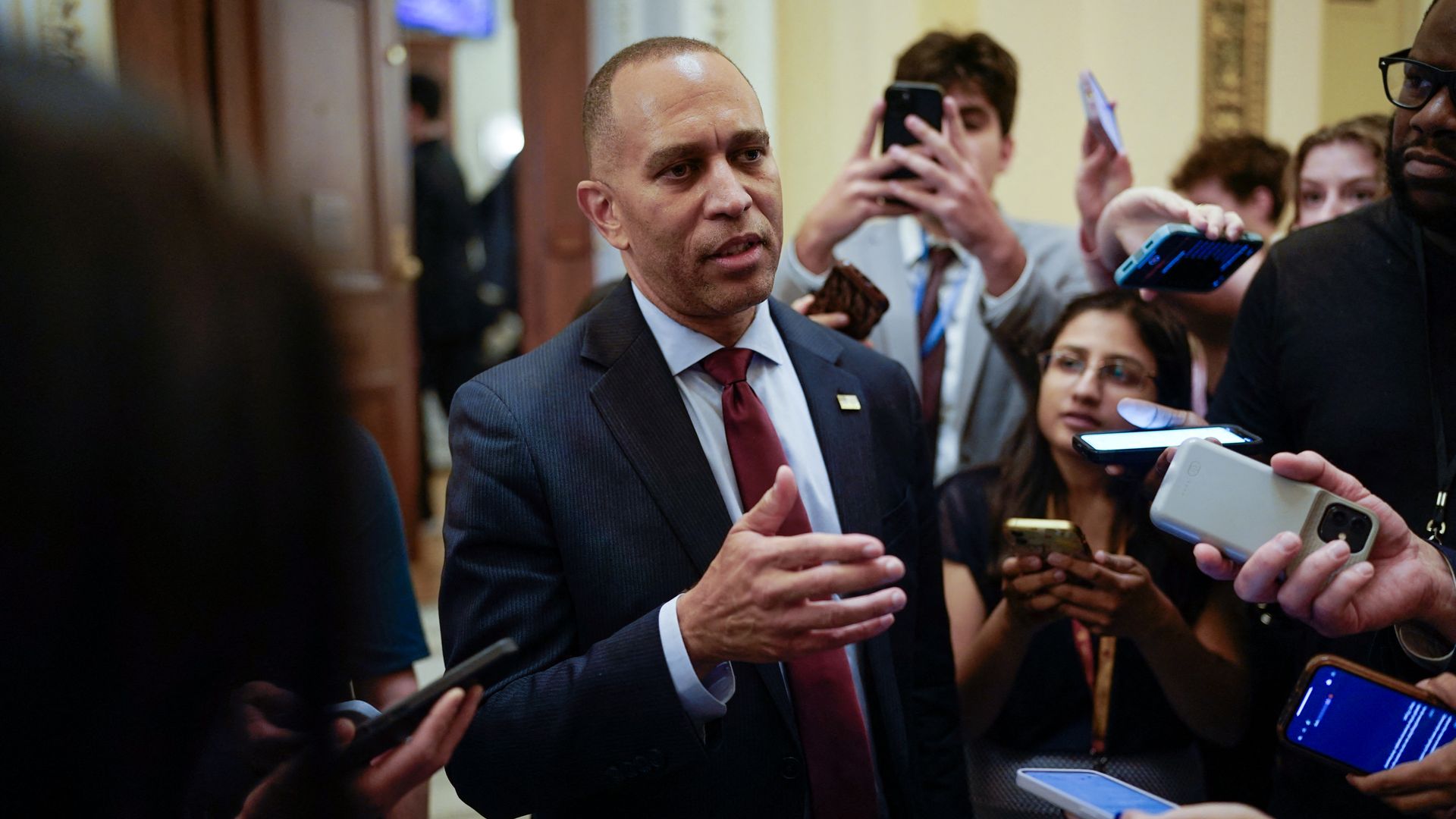 Hakeem Jeffries wearing a blue suit while surrounded by reporters taking photos and recording with their phones.