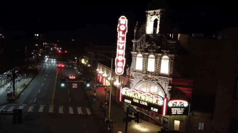 A gif showing a movie theater marquee on a boulevard, its signage lit up in lights.