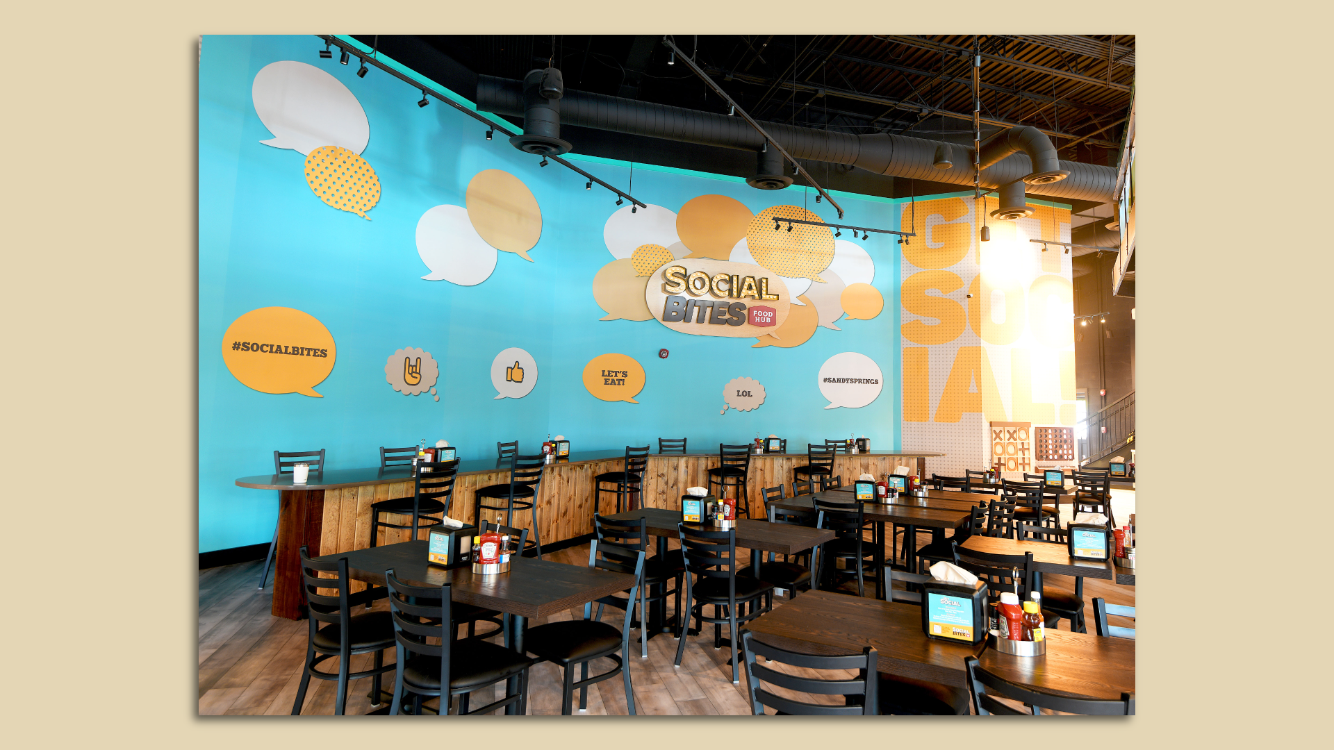 A photo of a restaurant with dark tables and a bright blue mural with orange bubbles, one of which says "Social Bites"