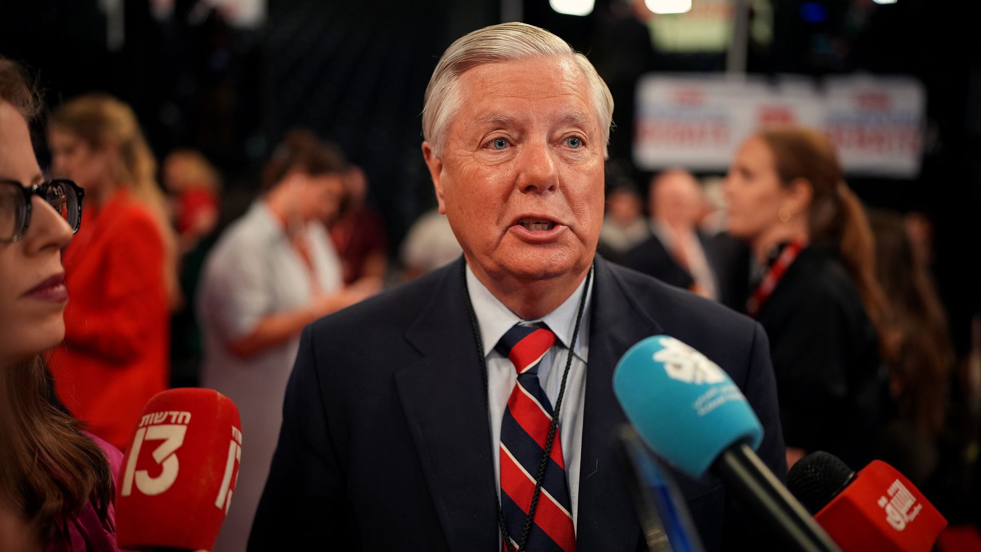 Sen. Lindsey Graham, wearing a gray suit and speaking into blue and red microphones.