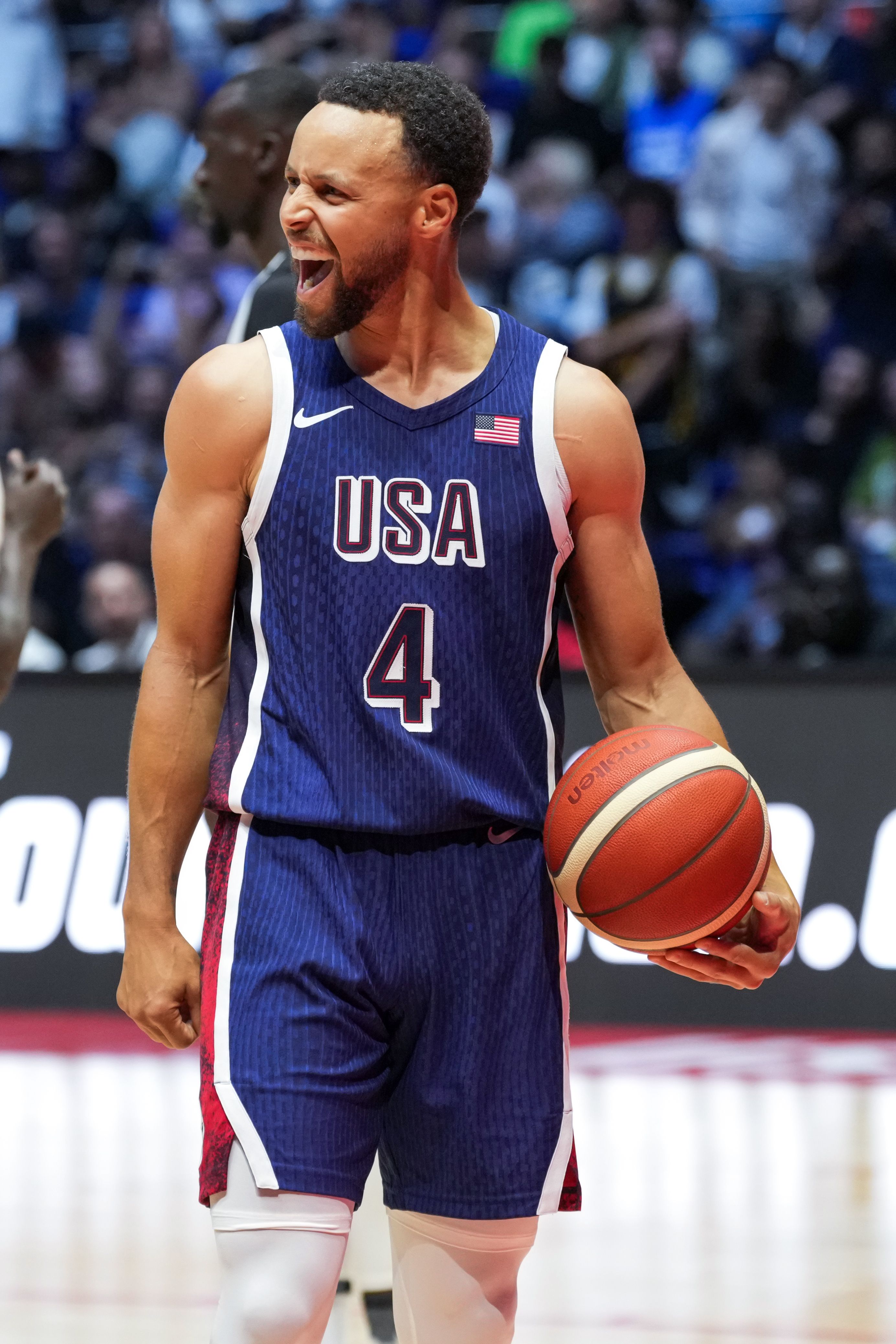 Steph Curry holds a basketball on a basketball court in a team USA uniform. 