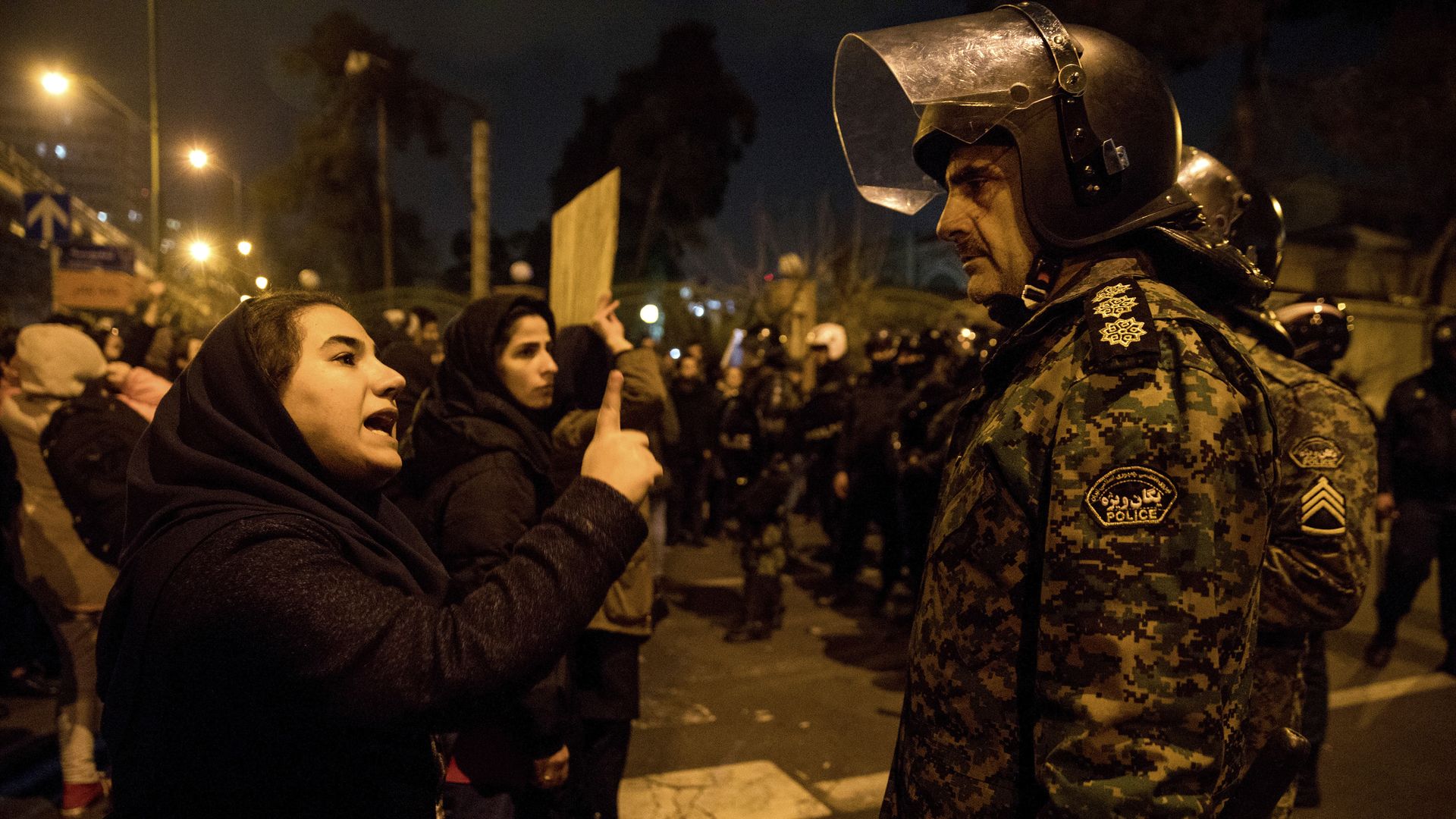 A woman attending a candlelight vigil for crash victims talks to a policeman, at the gate of Amir Kabir University in Tehran, where some of the victims studied.