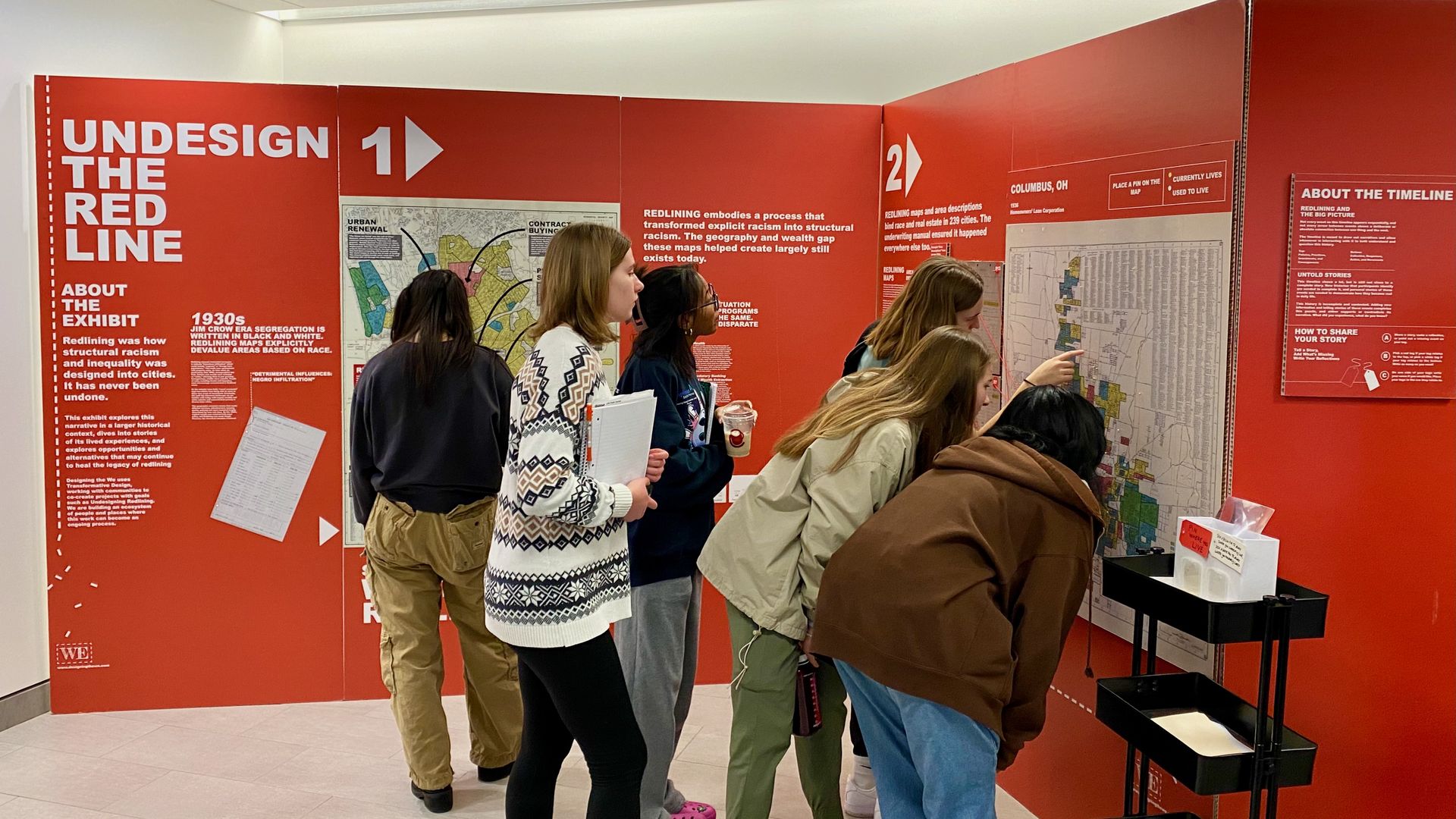 Students point on a map on a red display that reads "Undesign the Redline"