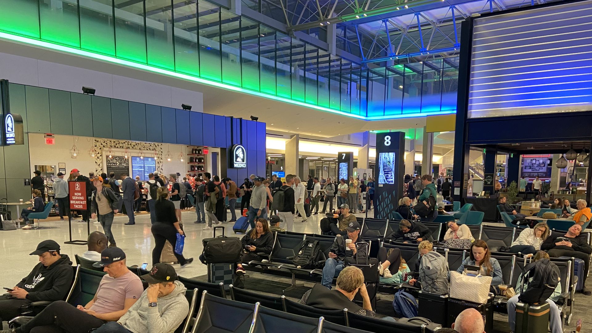 A photo of passengers waiting in seats with green and blue lights on the ceiling above them.