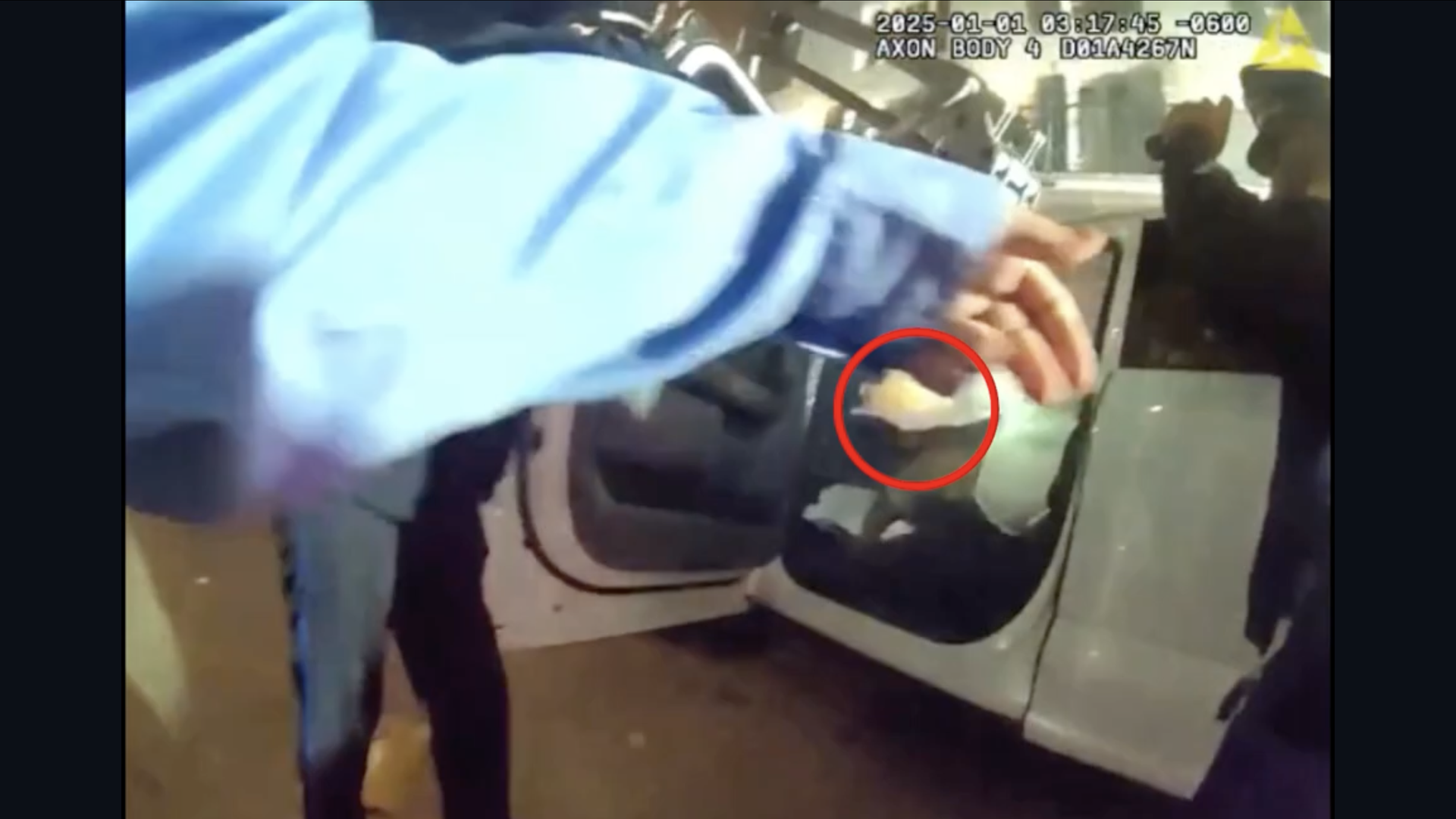 In a video still image, an NOPD officer approaches a white truck with the door open. The officer's arm and hand cover the driver's face, and a white flash is seen just below the officer's outstretched palm, as though it's in the driver's lap.