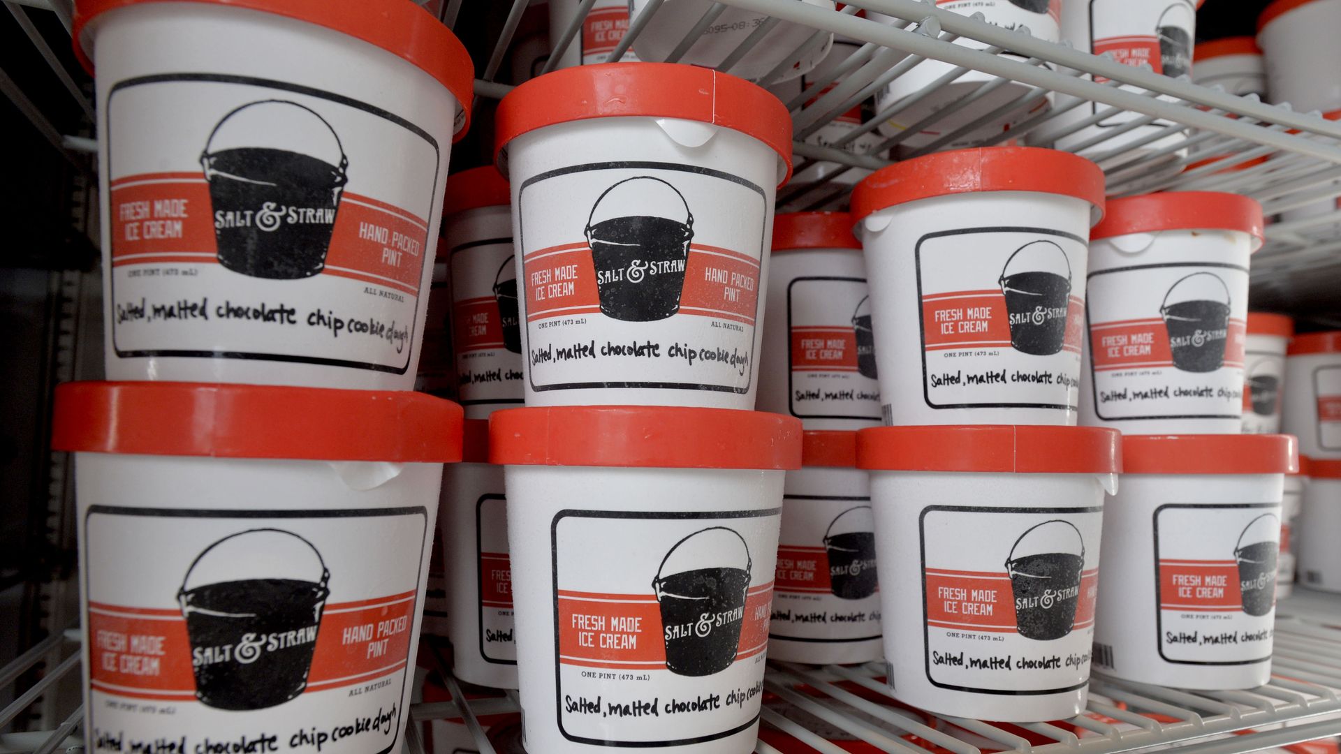 Close-up of stacked white ice cream cups with bright red lids on metal shelves, labeled Salt & Straw and Fresh Made Ice Cream.