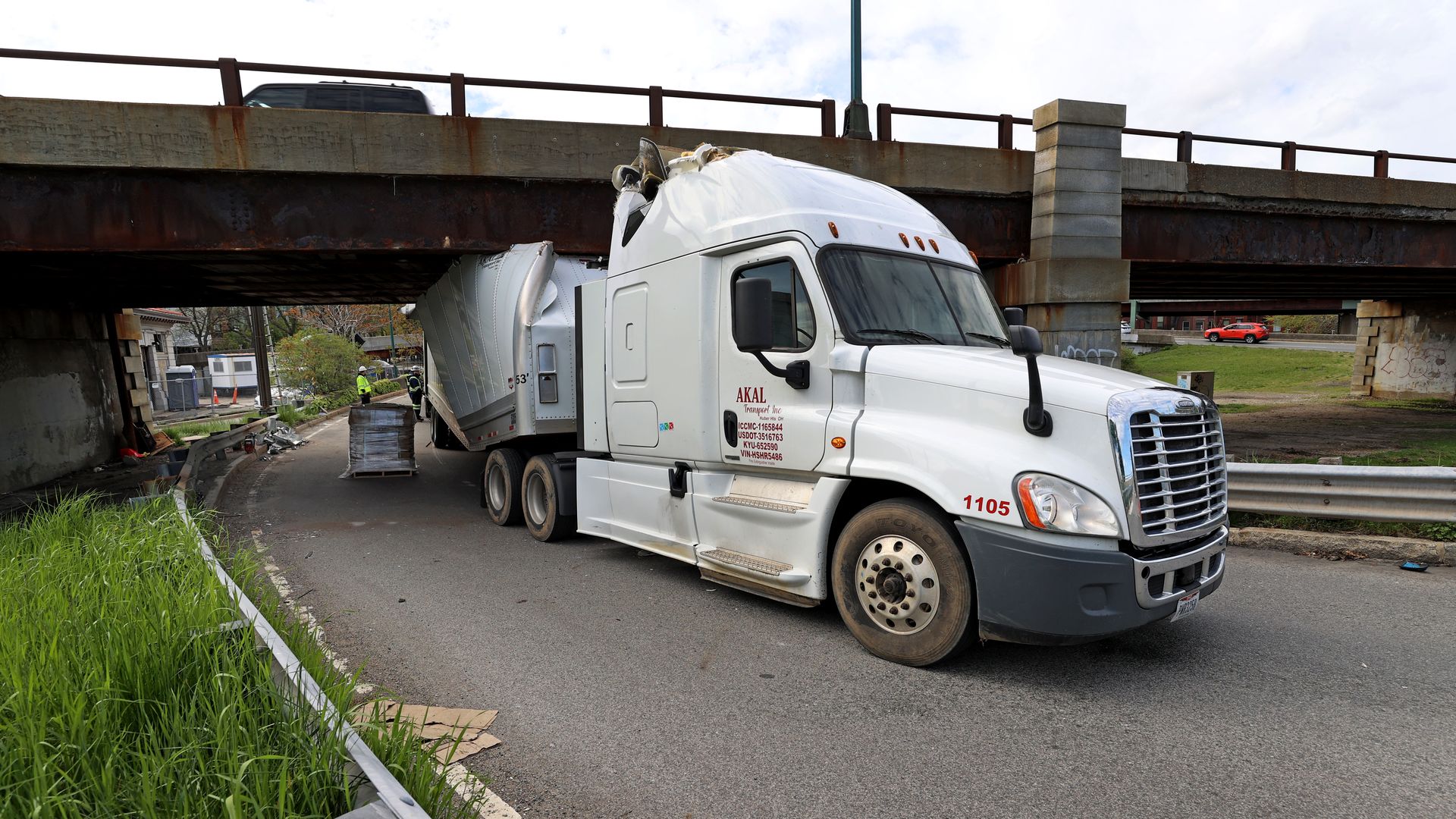 White semi-truck with crushed trailer stuck under a bridge on Storrow Drive.